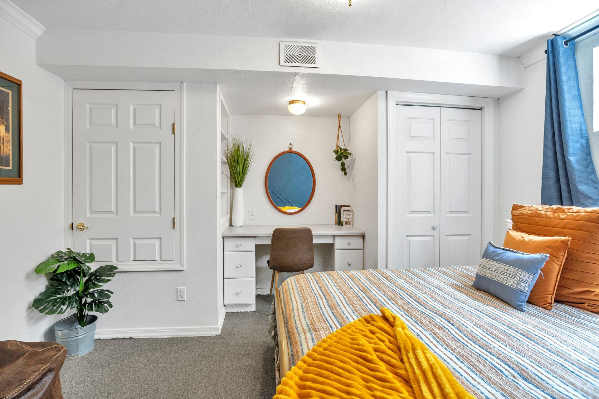 Bright bedroom with white walls, twin closets, desk, blue curtains, and a bed with orange and blue bedding