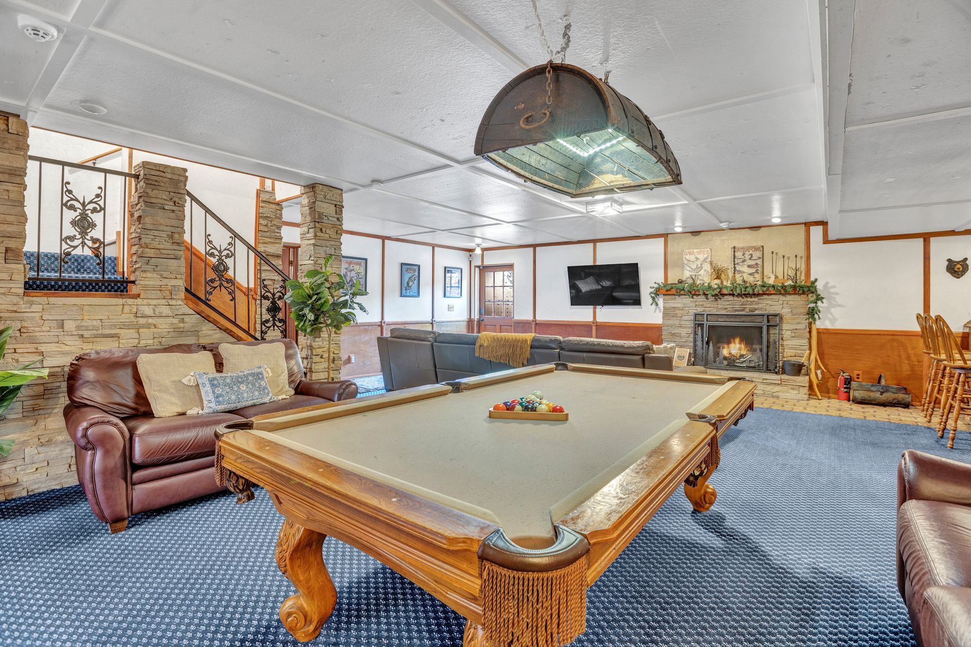 Recreation room with pool table, leather chair, TV, and staircase on a blue carpet.