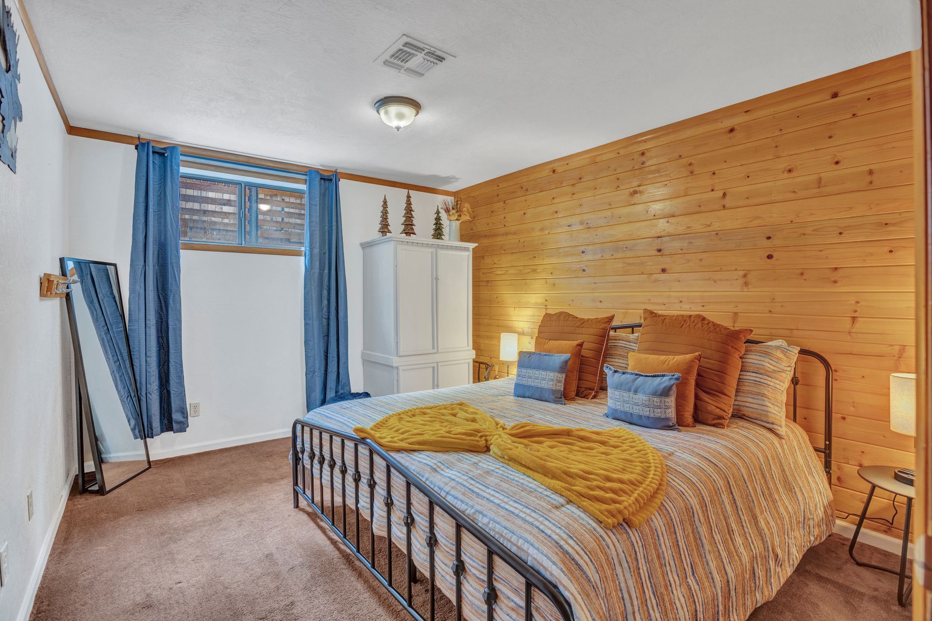 Small bedroom with a bed, blue curtains, white closet, and wood-paneled wall