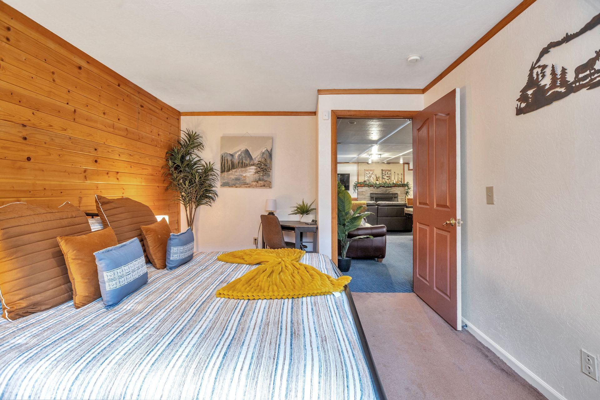 Bright bedroom with wooden accent wall, striped bed, yellow throw, and open doorway to another room