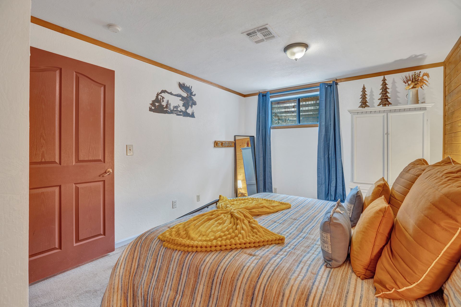 Small bedroom with a bed, white walls, red door, and window with blue curtains.