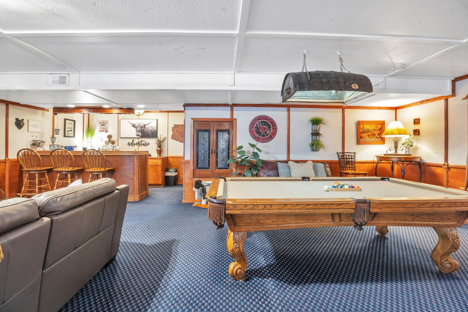 Recreation room with pool table, wood bar, sofa, and blue carpet under fluorescent lights
