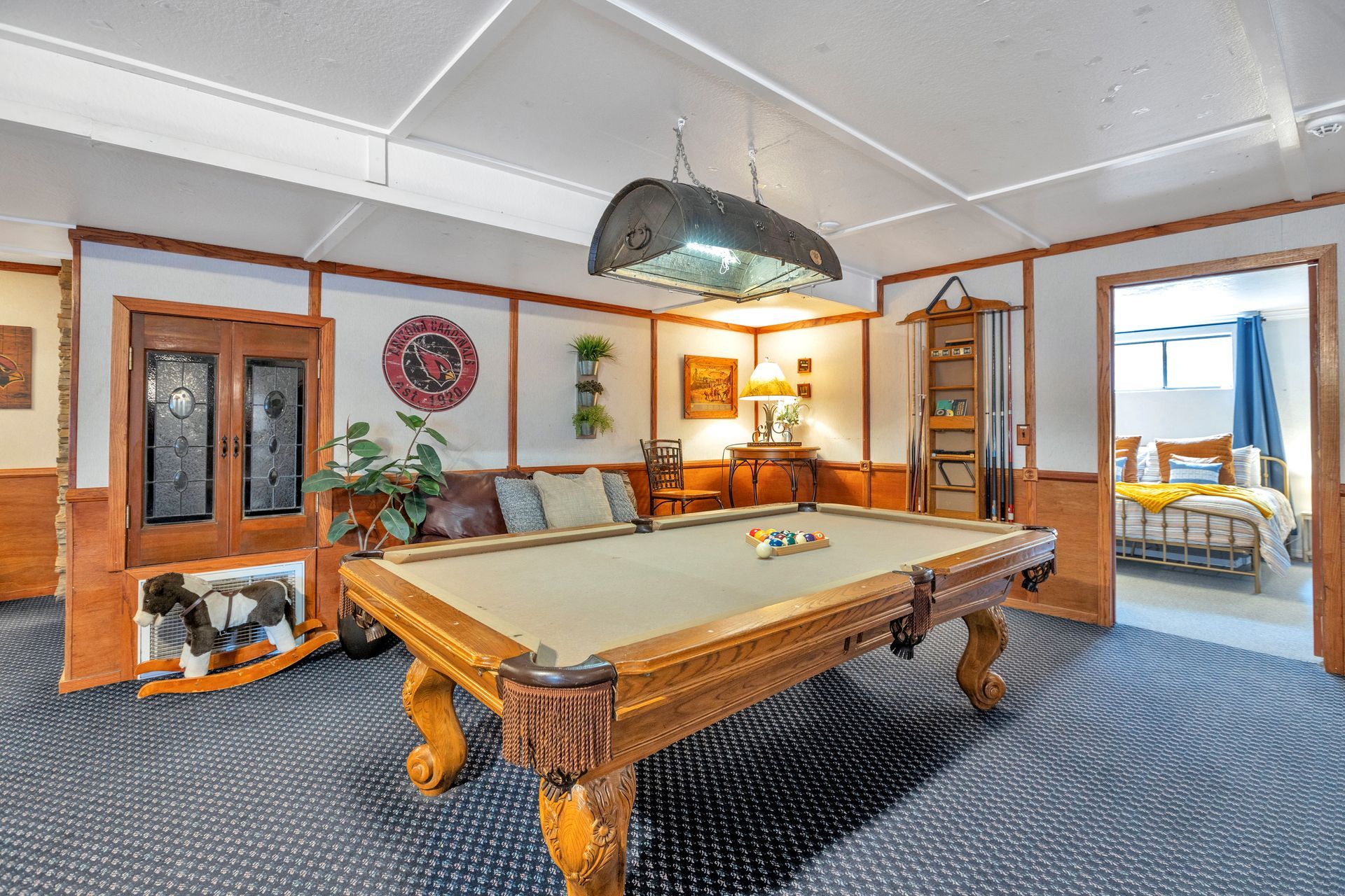 Spacious game room with pool table, wood cabinets, patterned carpet, and a doorway to a bright adjacent room