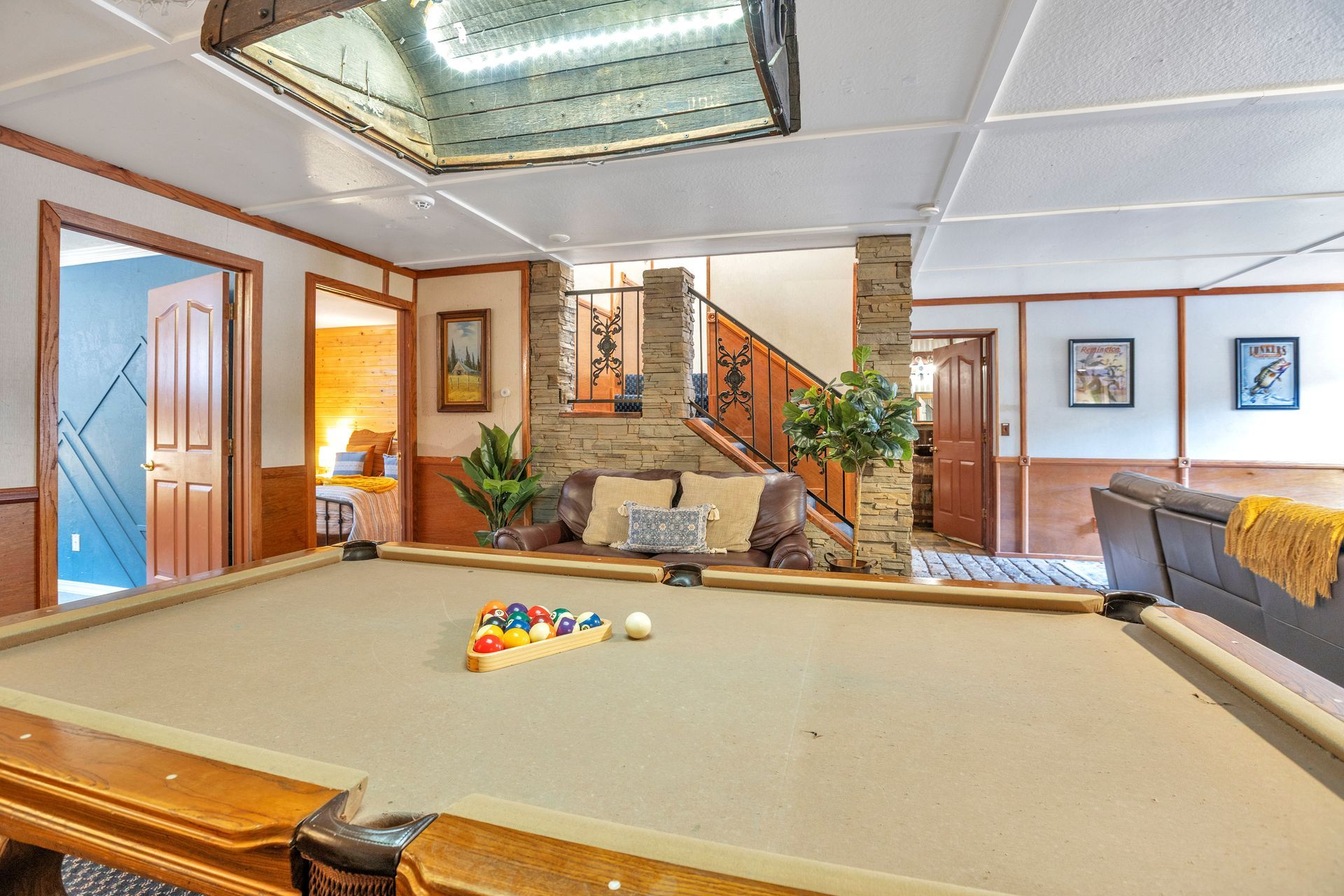 Spacious recreation room with a pool table, brick fireplace, staircase, and warm wood accents