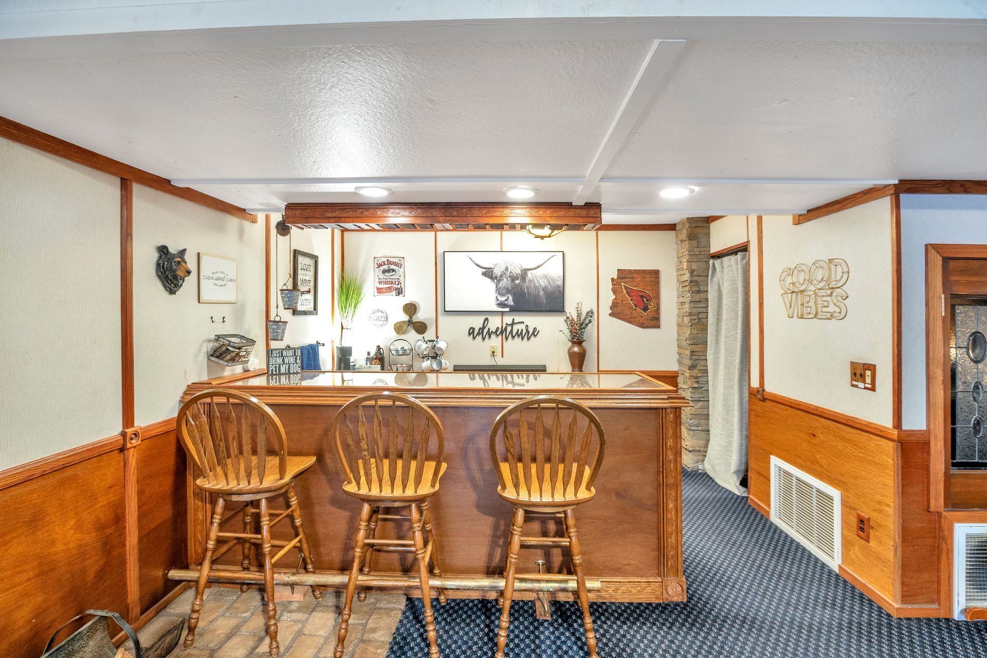 Wood-paneled basement bar with three stools, countertop, and recessed lighting