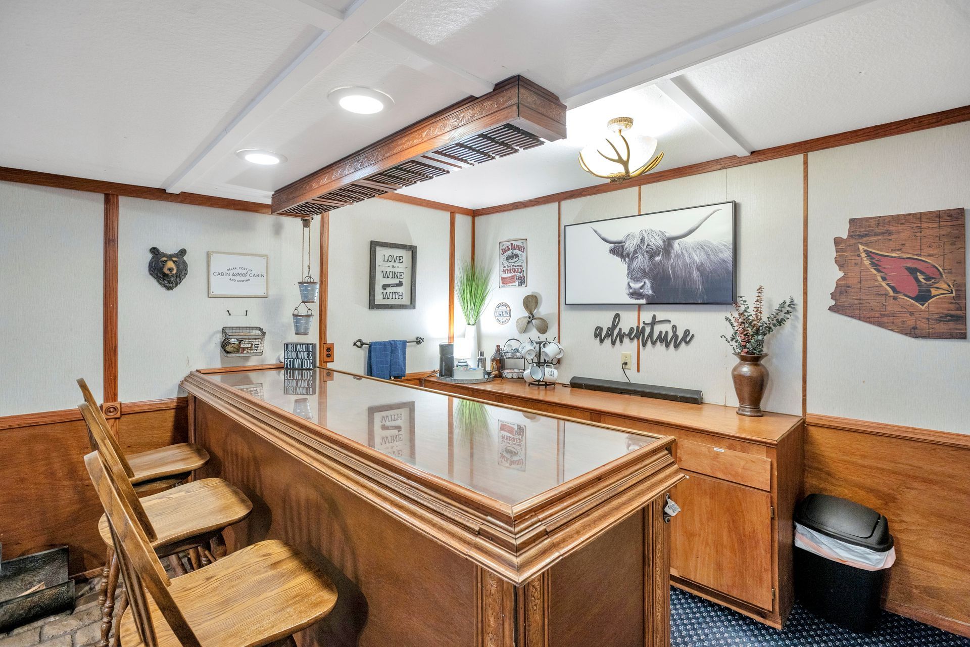 Cozy wood-paneled bar nook with stools, overhead rack, and framed wall art