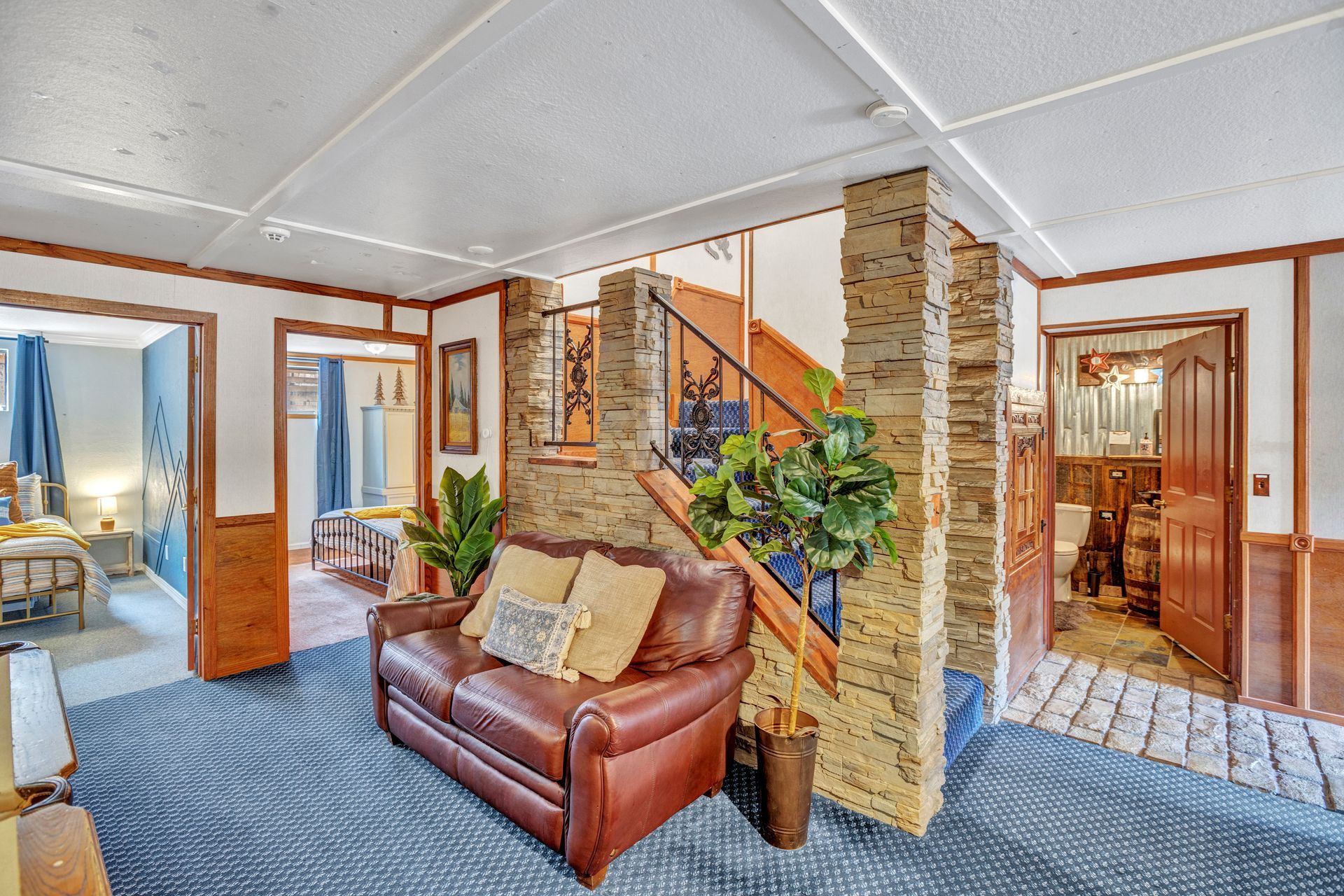 Bright living room with leather sofa, brick walls, staircase, and blue patterned carpet