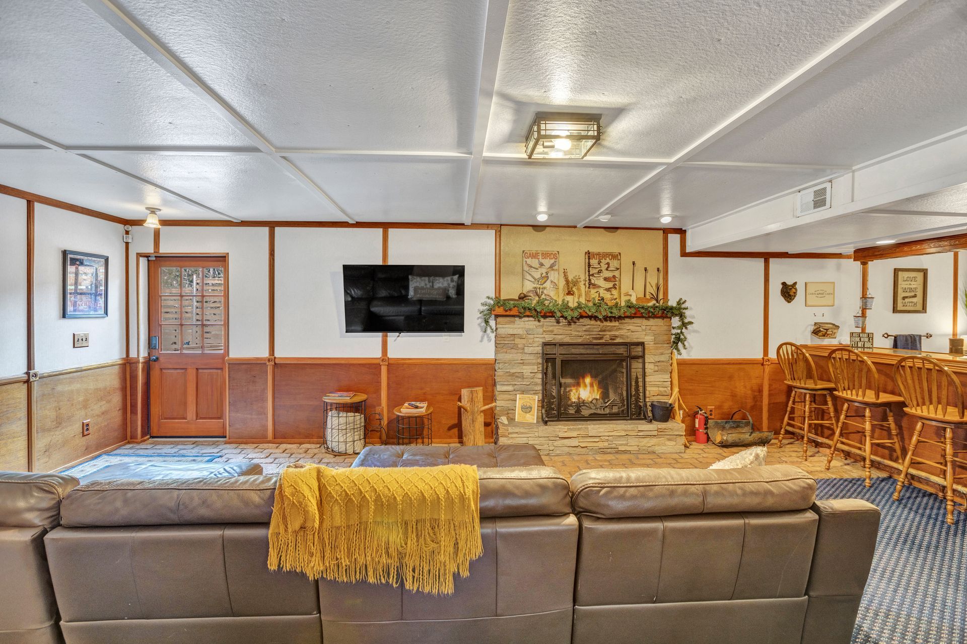Cozy living room with leather sectional, fireplace, wall TV, and wood-paneled walls