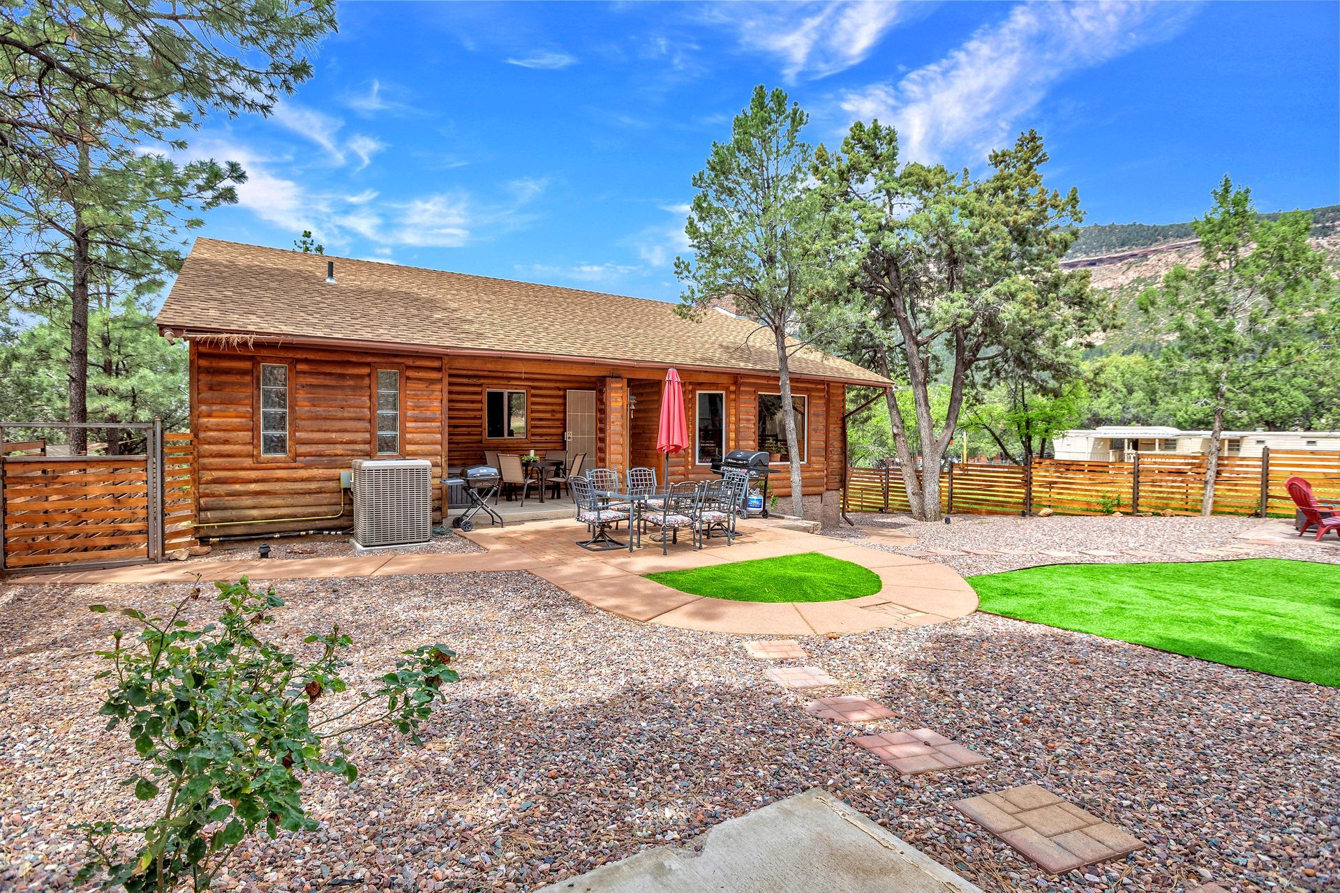 Log cabin home with stone patio, landscaped yard, and blue sky on a sunny day