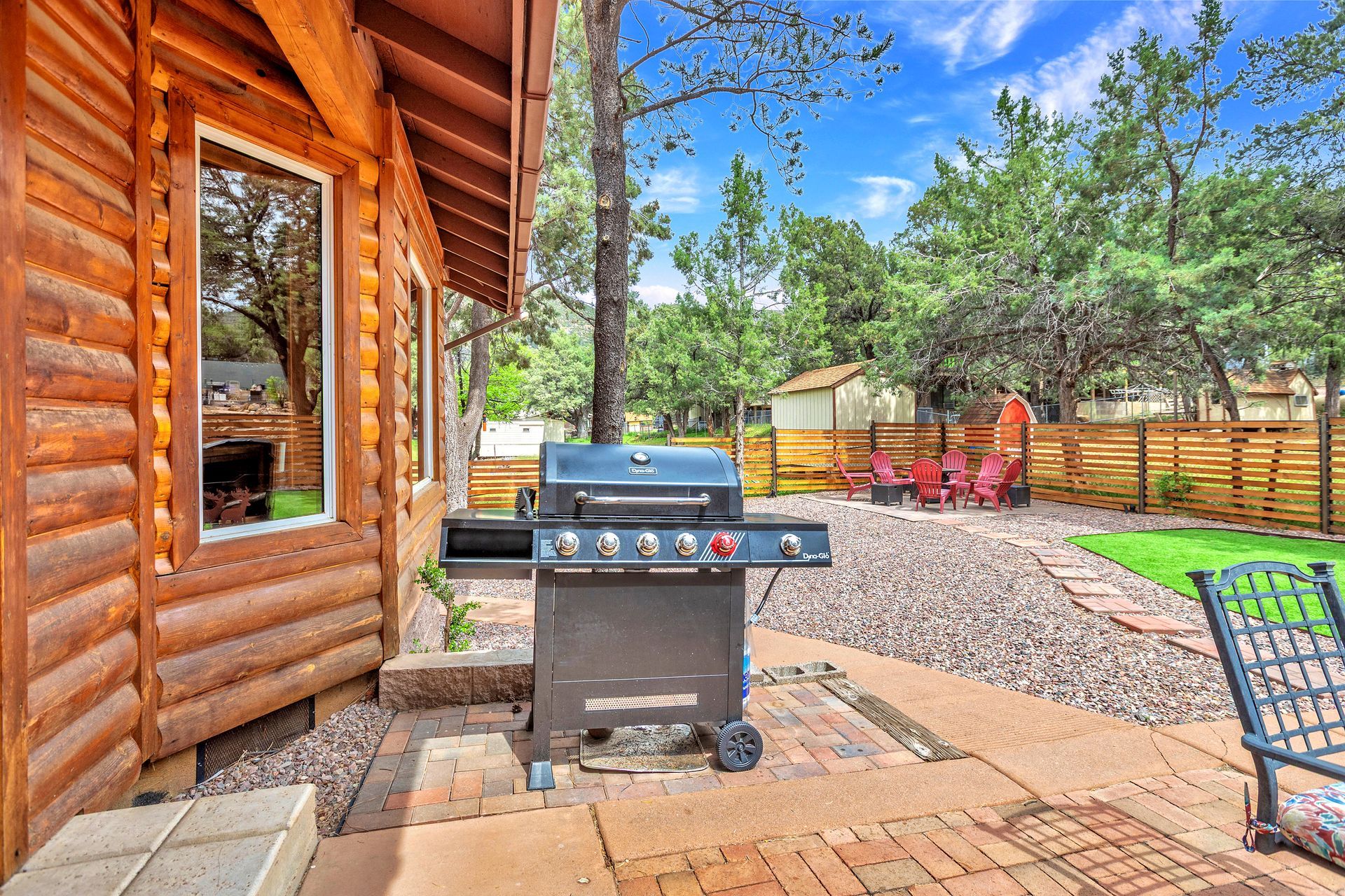 Wooden cabin patio with a stainless steel grill, paver stones, and trees in a fenced yard