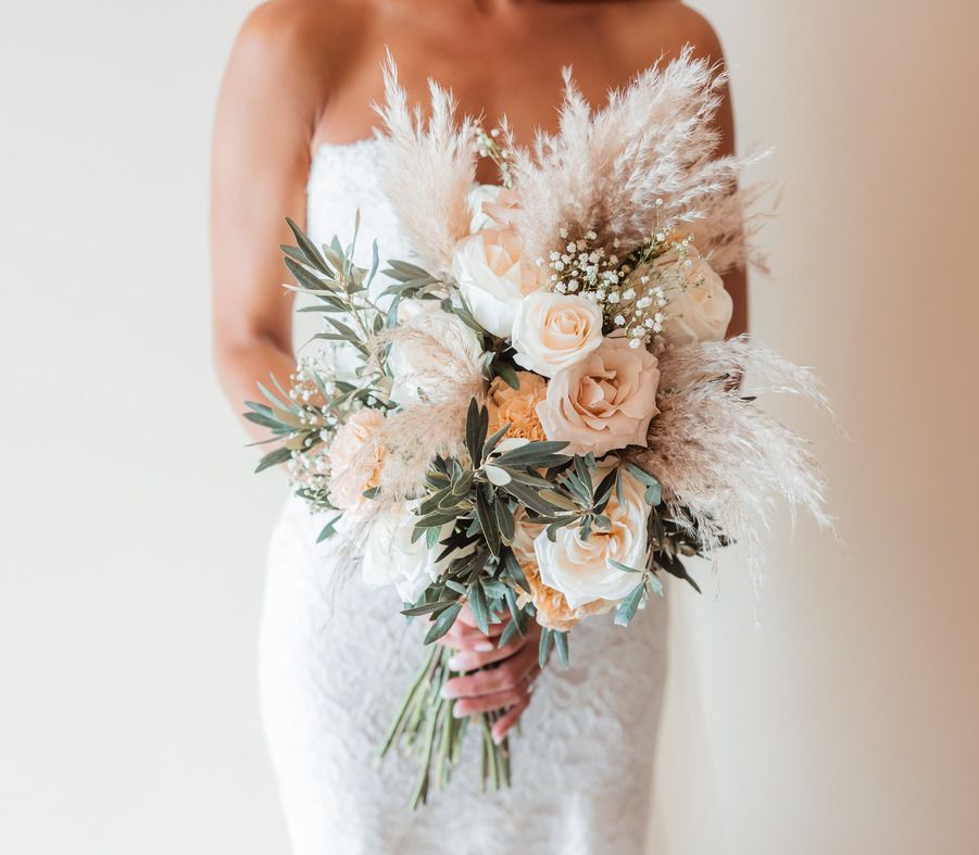 Bride in a white dress holding a bouquet of pale peach roses and dried white foliage
