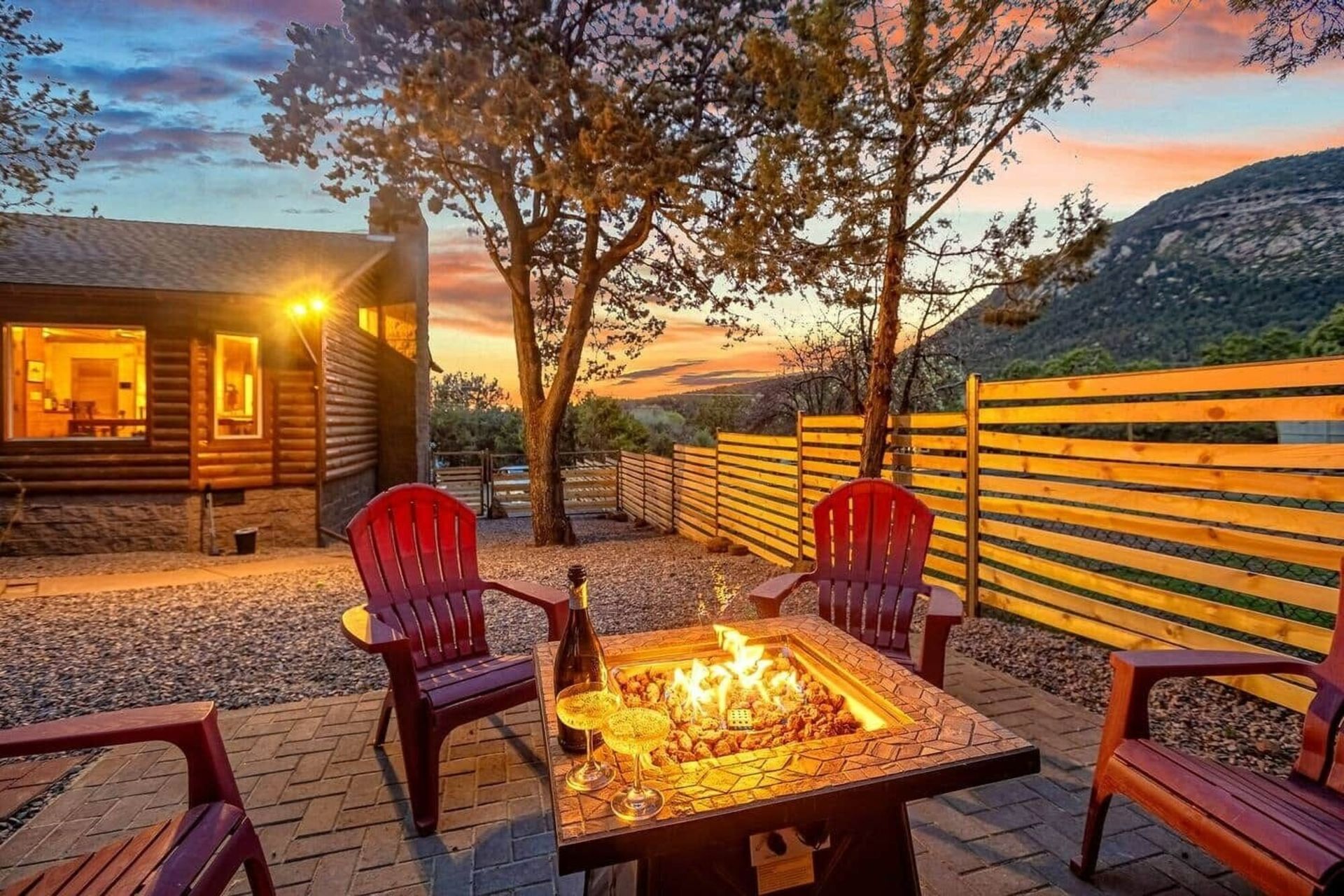 Cozy fire pit patio at sunset with red chairs, cabin lights, and mountain view