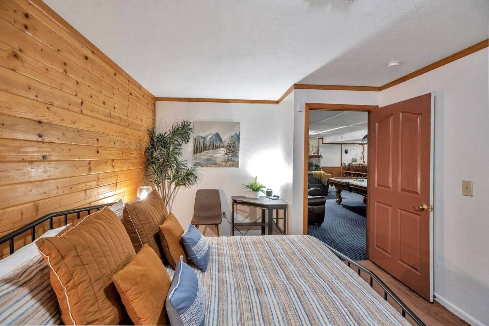 Bedroom with wood-paneled wall, bed, desk, and an open door to a hallway and living area.