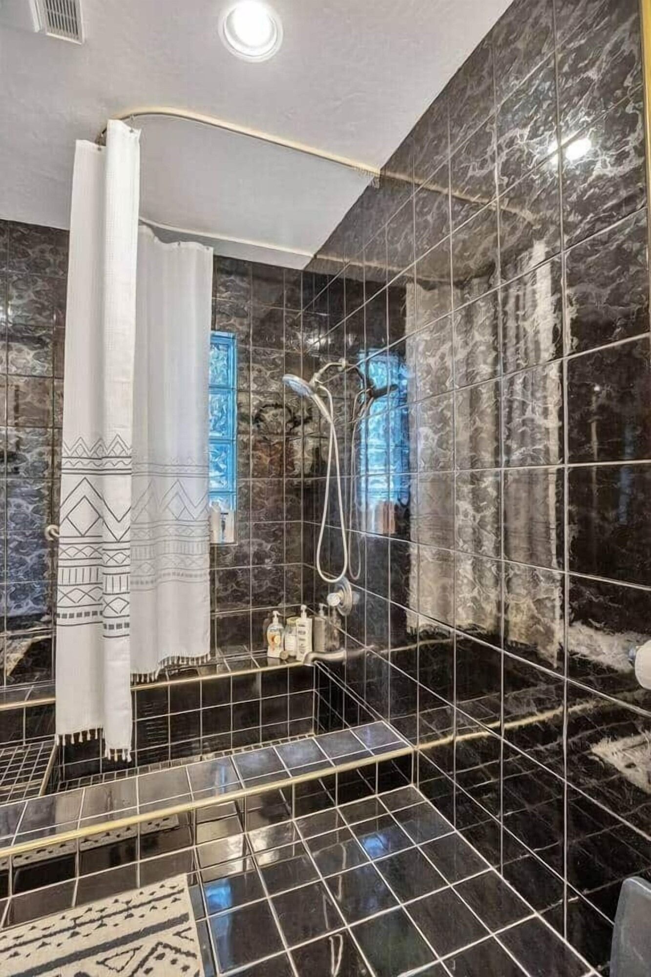 Modern bathroom with glossy black tile, a bathtub, shower curtain, and mirrored vanity area.