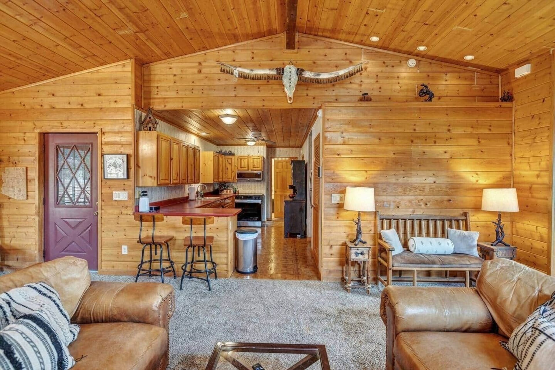 Wood-paneled cabin living room with leather sofas, a kitchen bar, and a mounted fish decor