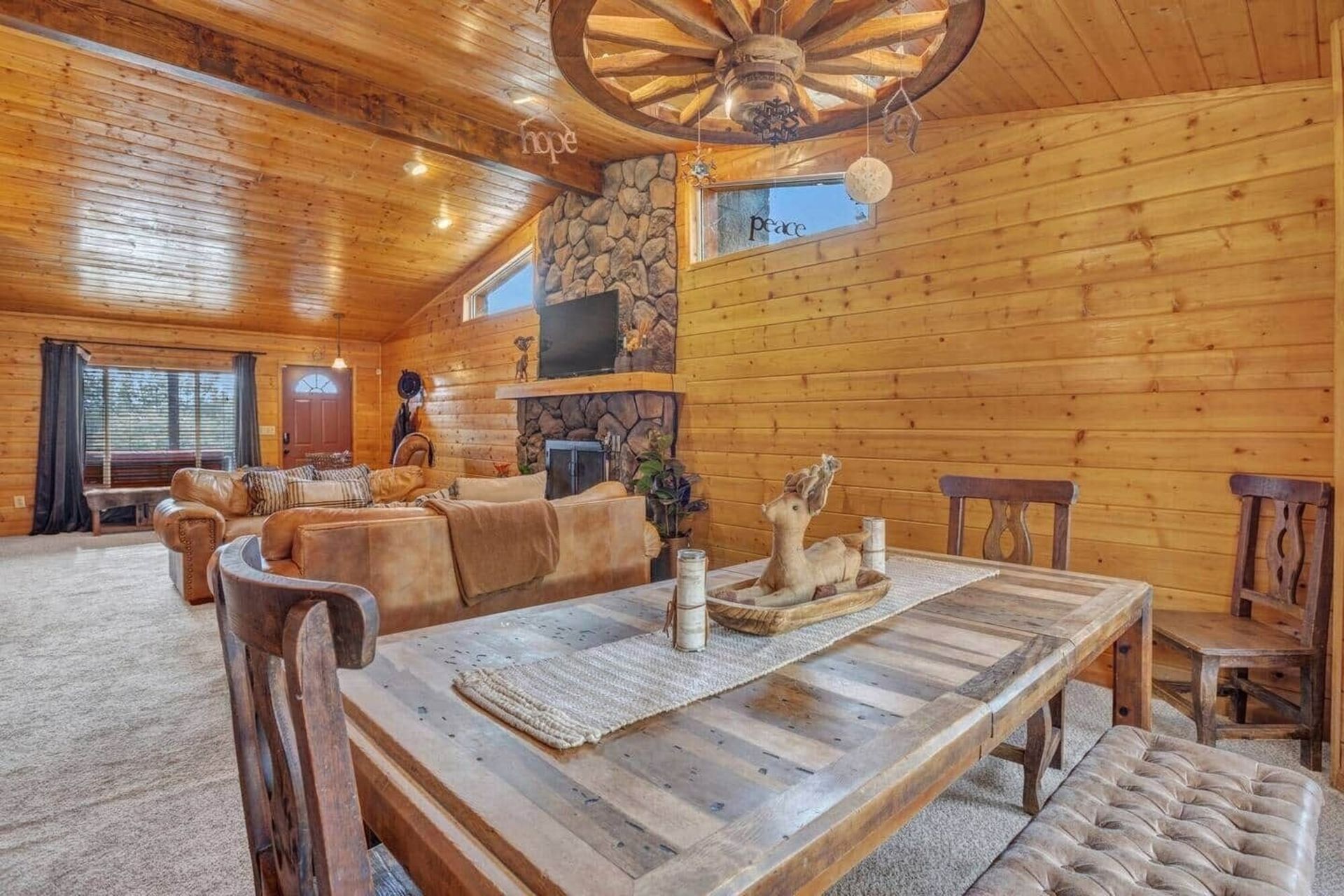 Cozy wood-paneled living room with rustic furniture, stone fireplace, and vaulted ceiling chandelier