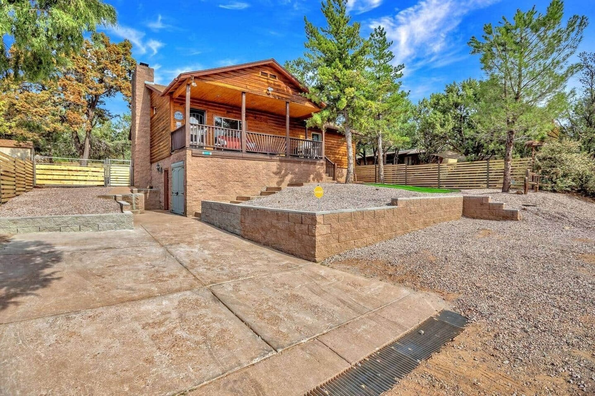Brick house with a covered porch, stone patio, and gravel yard surrounded by trees