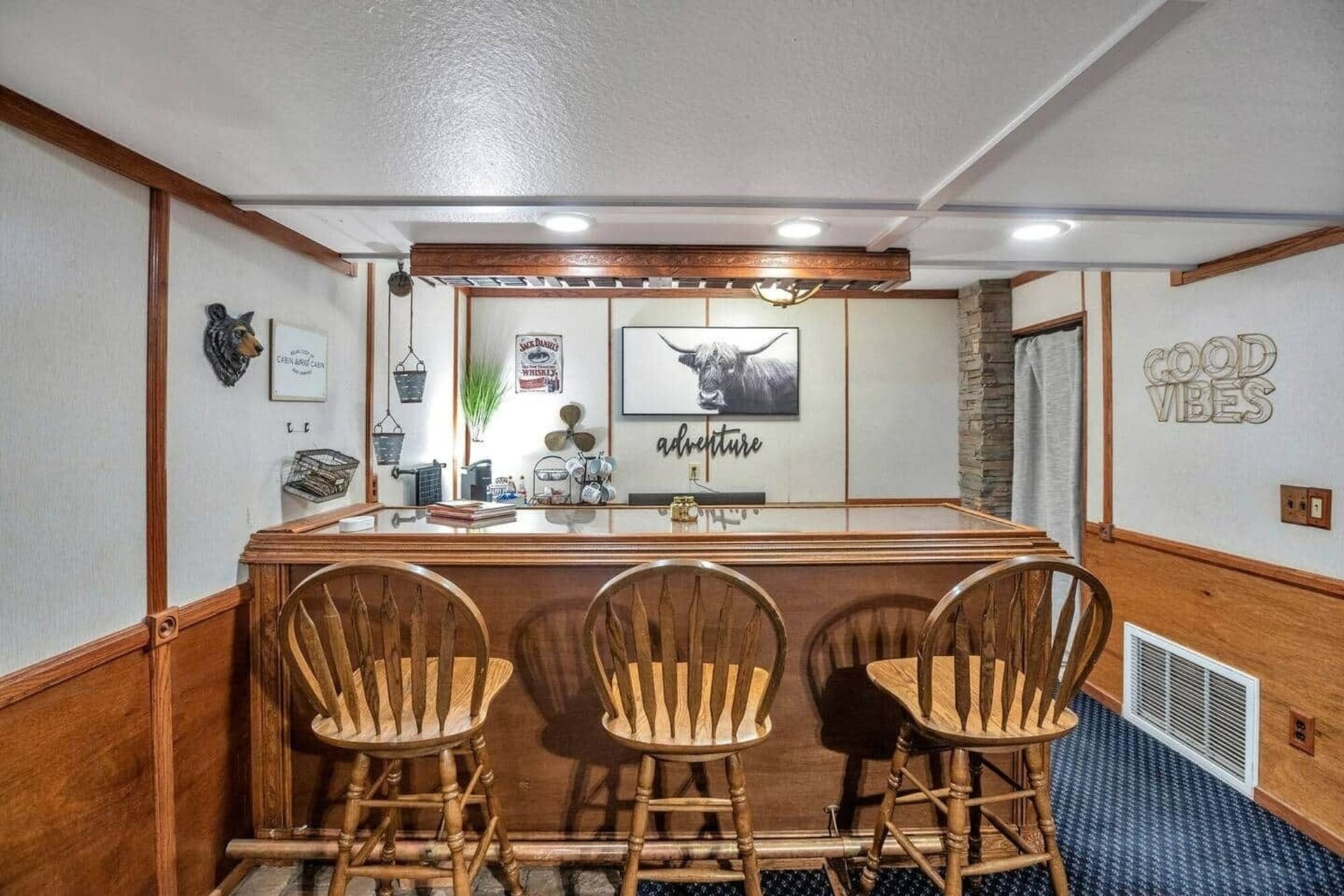 Wood-paneled basement bar with three stools, wood counter, and mounted deer art