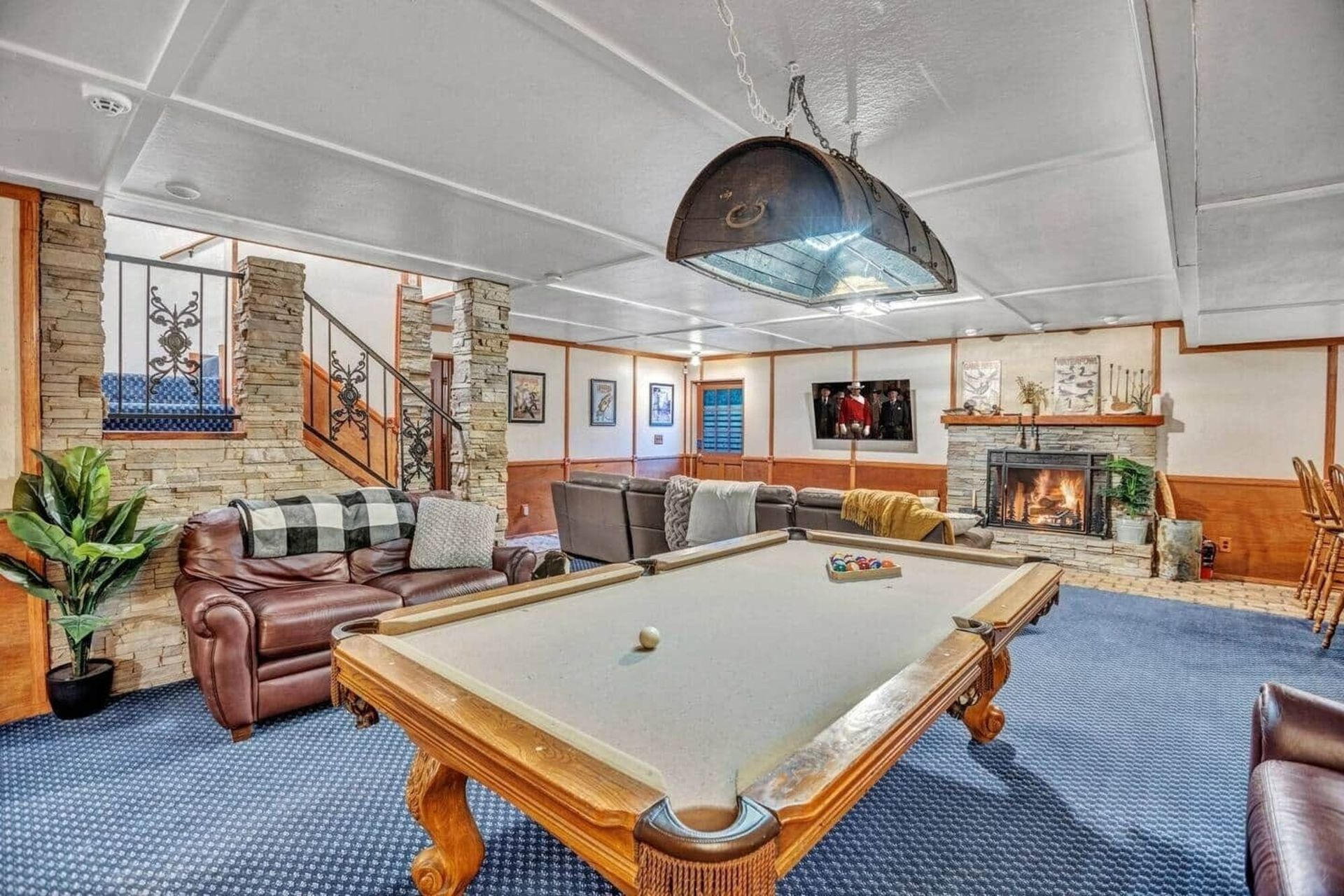 Spacious game room with a pool table, leather seating, fireplace, and wall art under a vaulted ceiling.