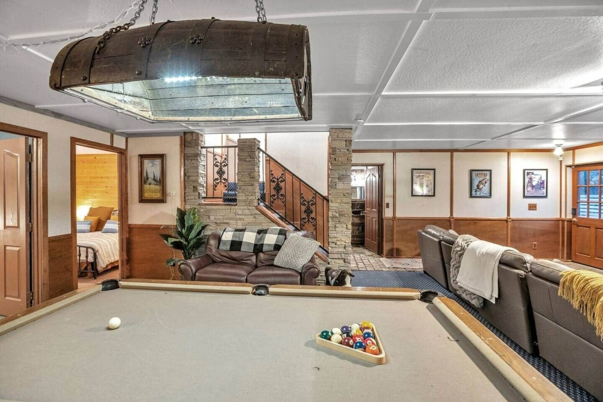 Spacious basement rec room with pool table, couch, staircase, and framed wall art