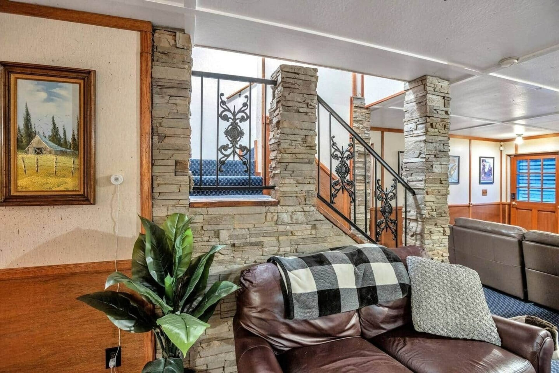 Modern living room with stone columns, leather sofa, potted plant, and staircase by windows