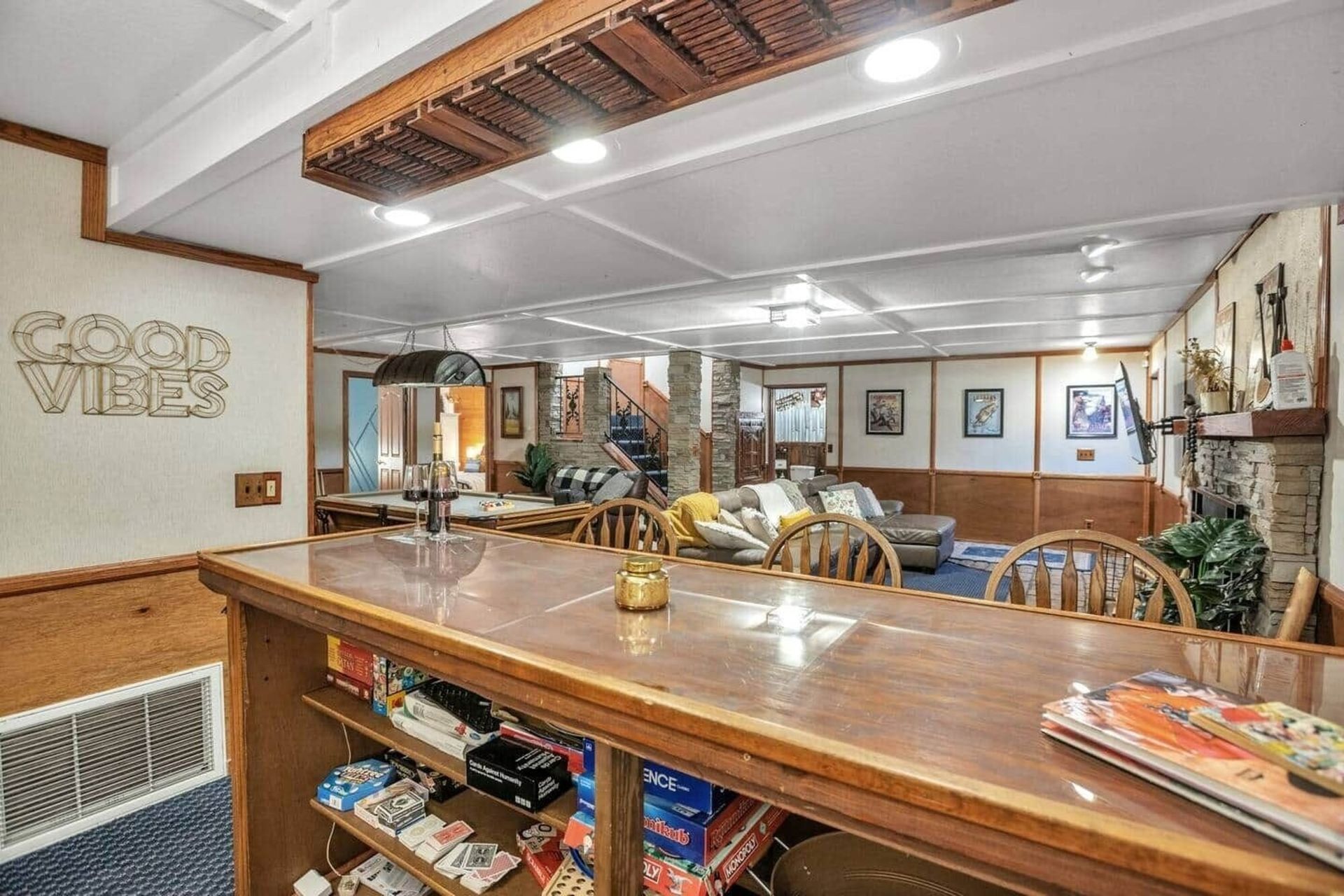 Wooden bar in a cozy basement game room with seating, ceiling lights, and wall decor