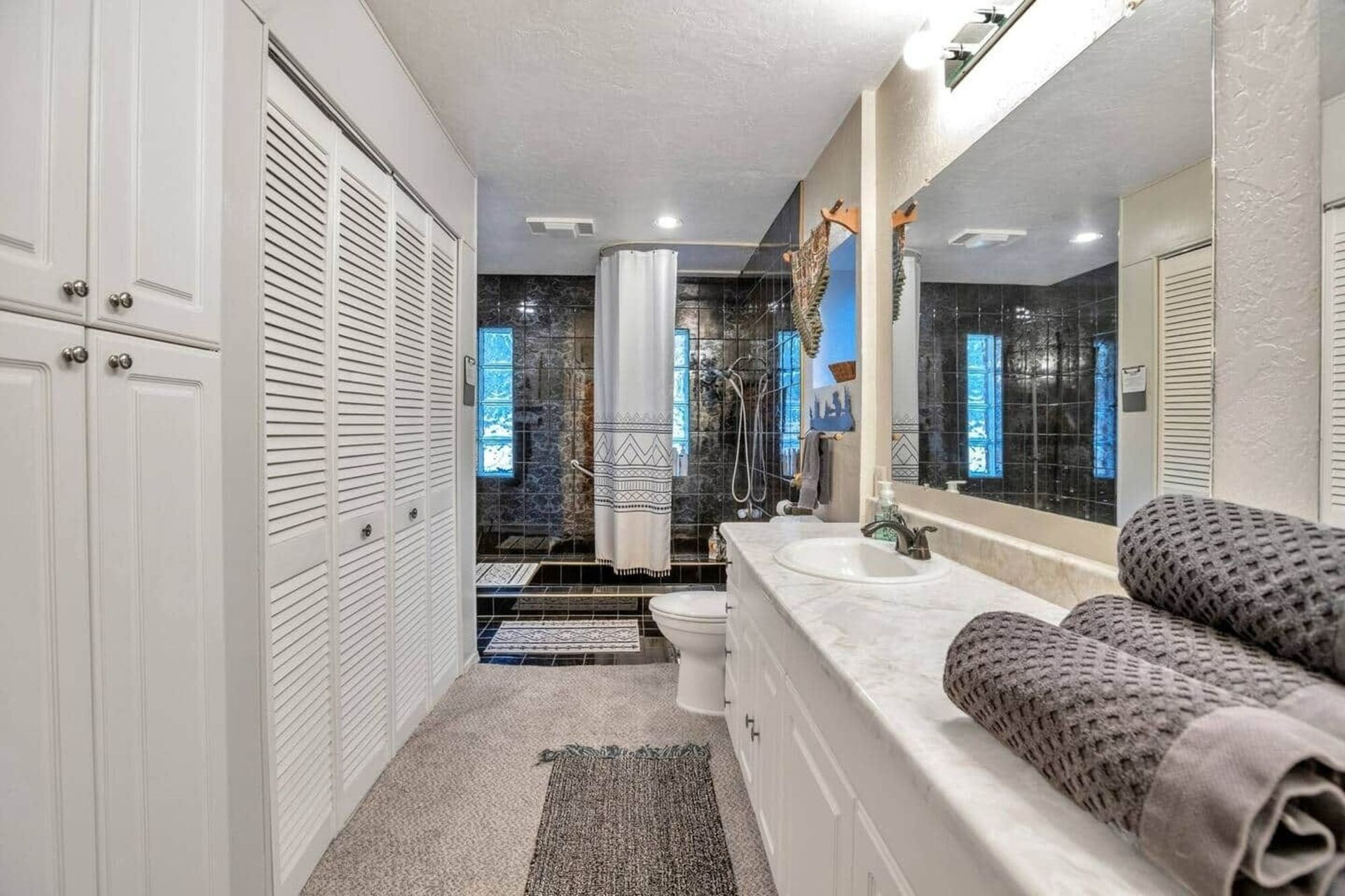 Bright bathroom with double sink, large mirror, white cabinets, and gray towels on the counter
