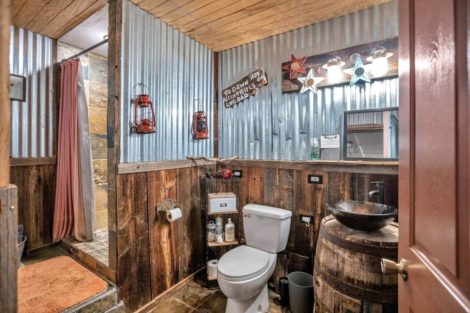 Rustic bathroom with corrugated metal walls, wood accents, toilet, and barrel-style sink.
