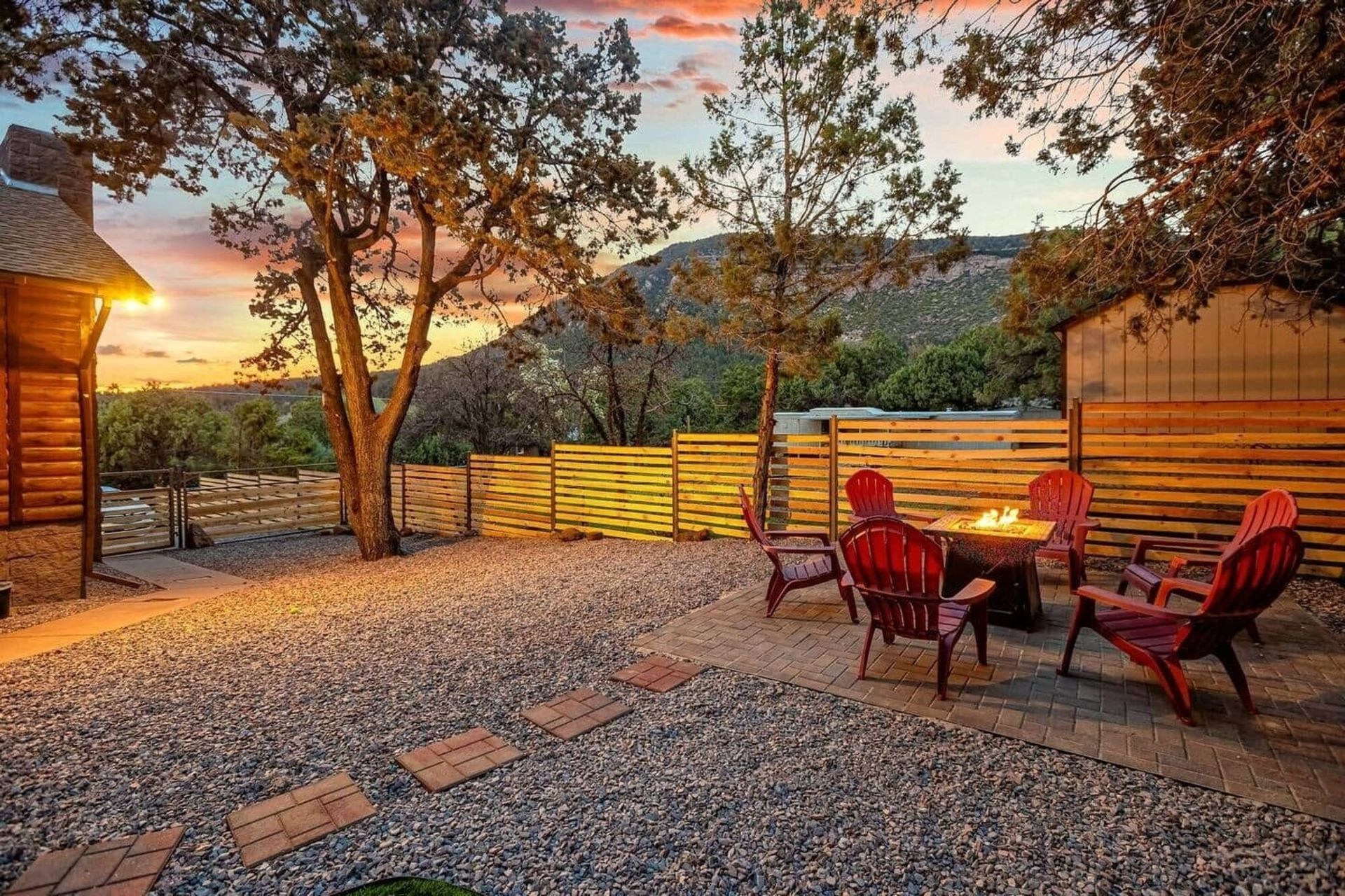 Backyard patio with red chairs, a table, string lights, and sunset views over hills