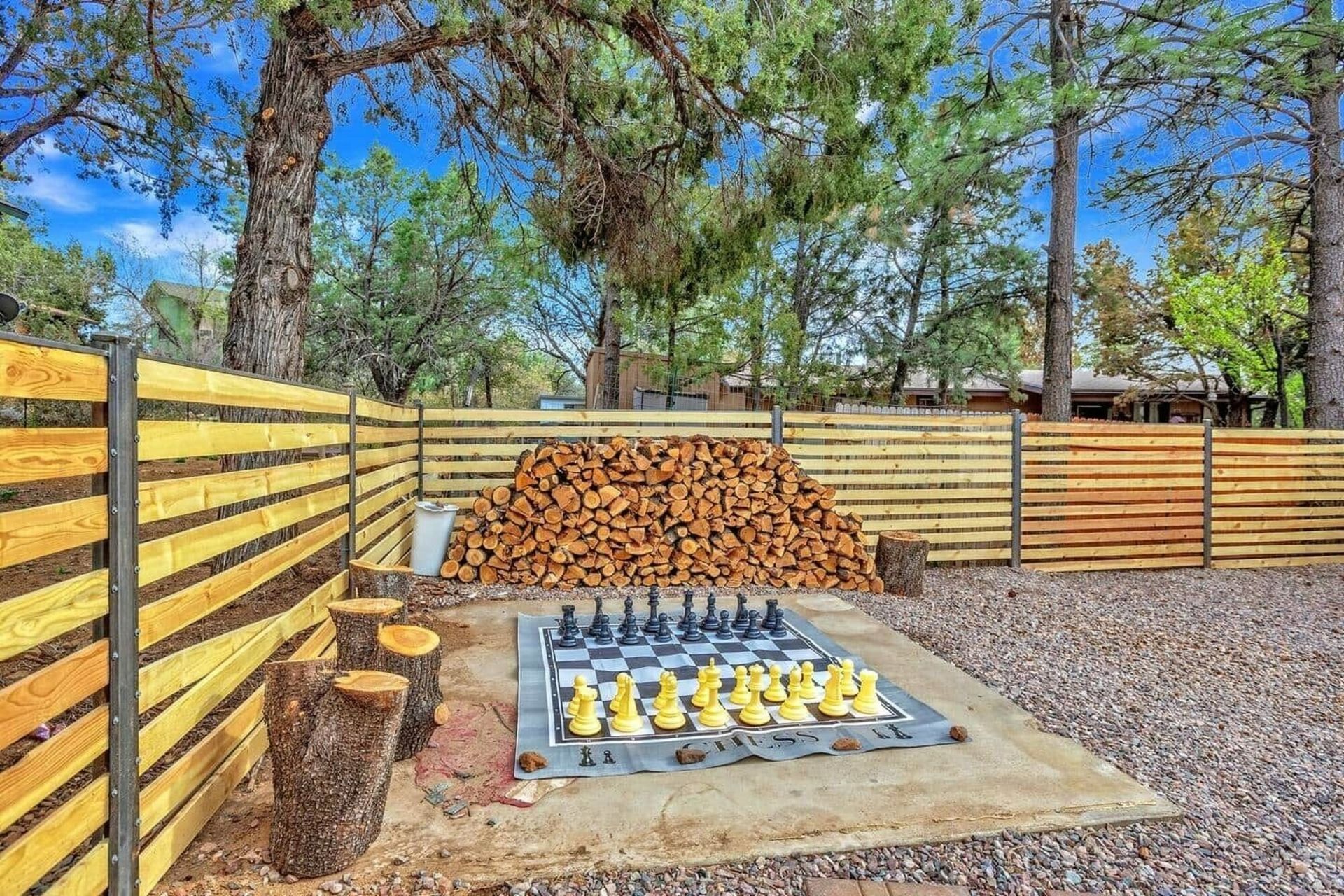 Backyard fire pit with logs, benches, and a wood-slat fence under trees
