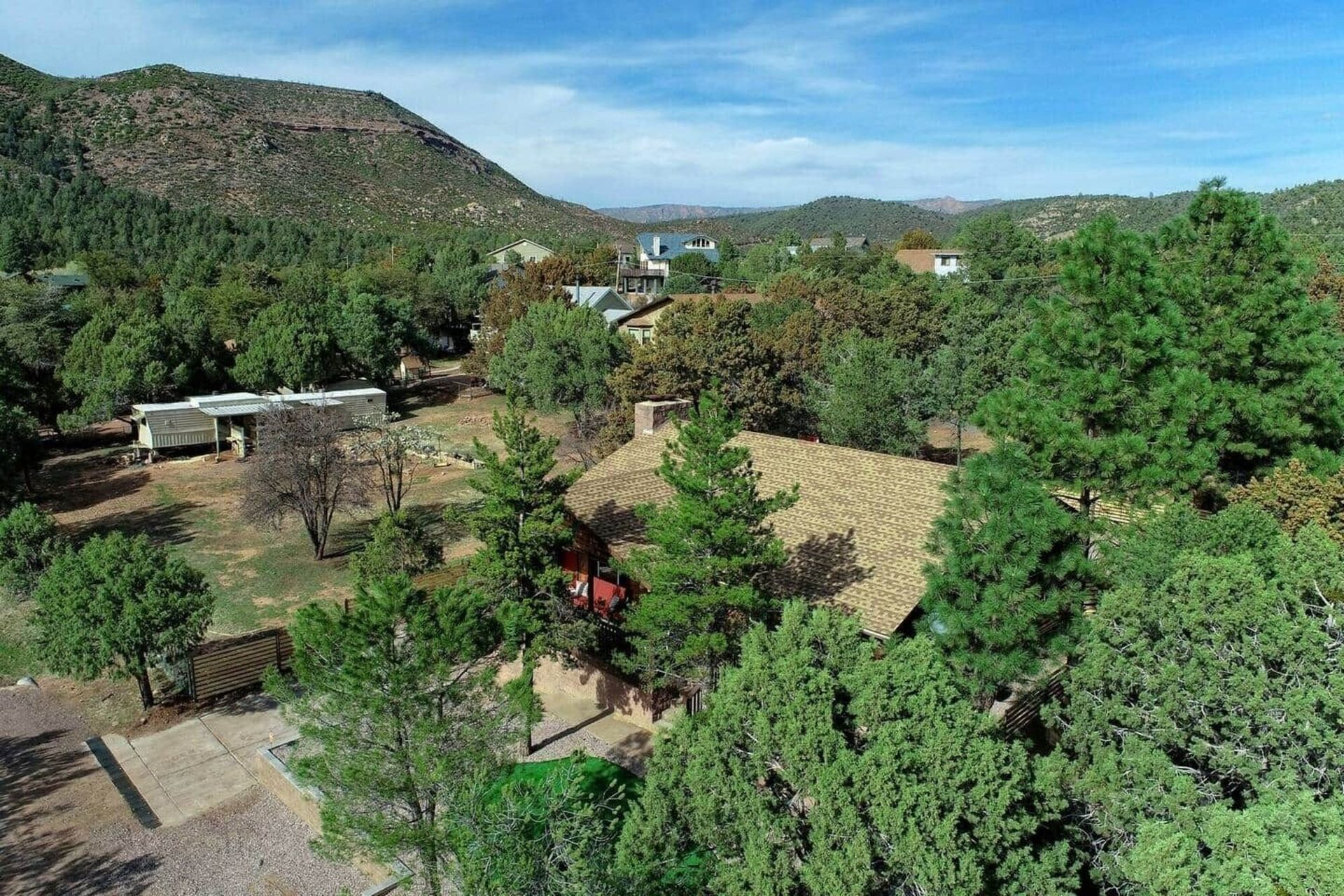 Rural hillside village with trees, stone buildings, and mountains under a clear blue sky