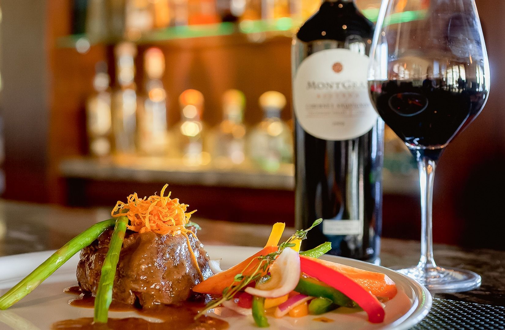 Wine glass and bottle beside a plated gourmet meal in a warm restaurant setting