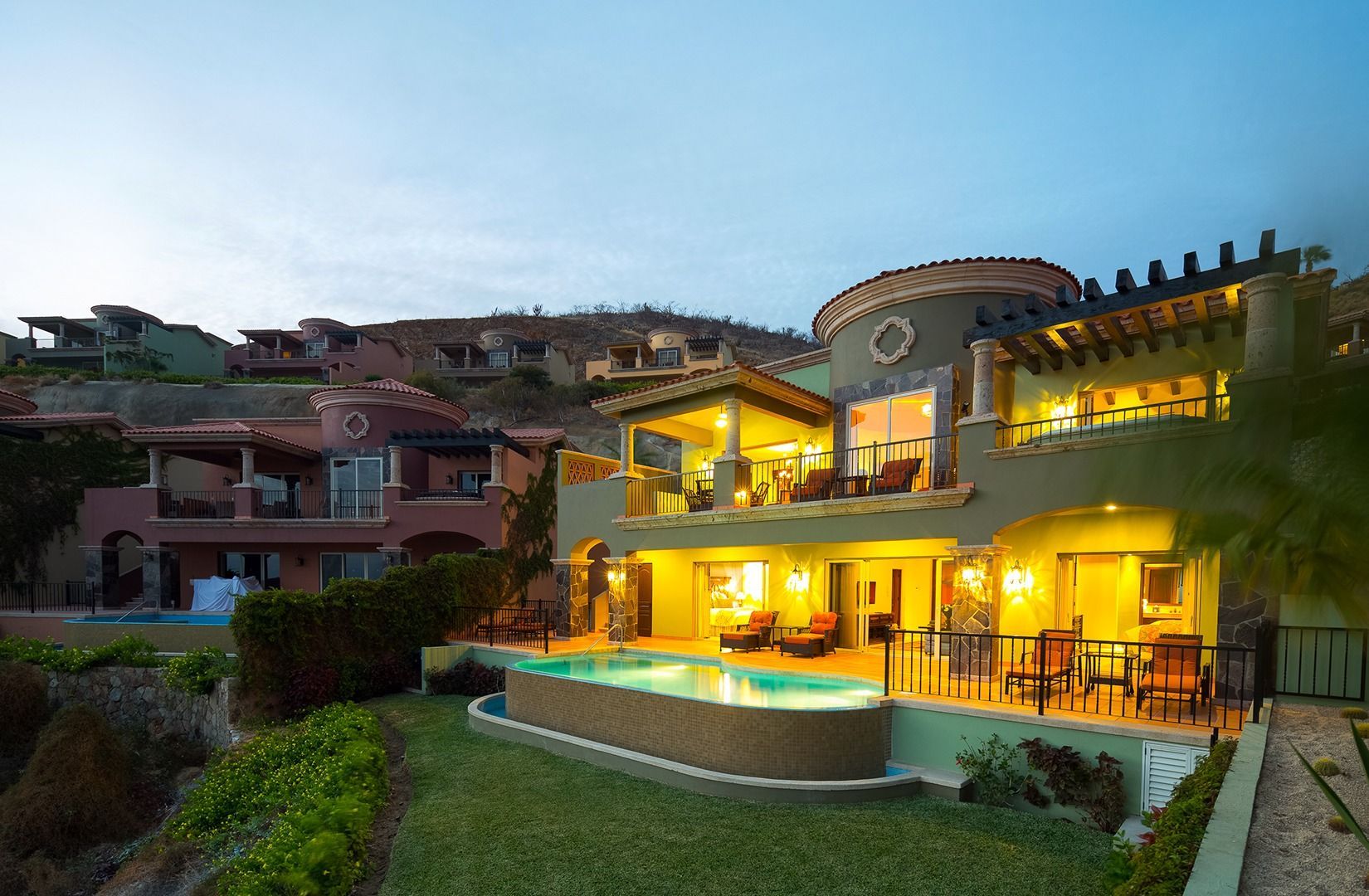 Luxury hillside villa at dusk with warm lights, pool, and ocean view