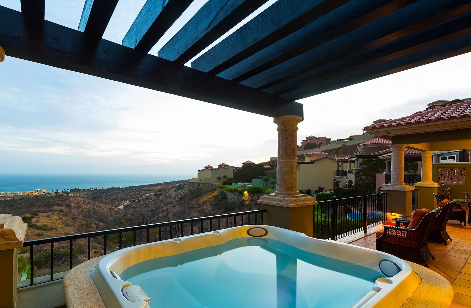 Patio with a hot tub overlooking the sea at sunset, beside a colorful house and covered terrace