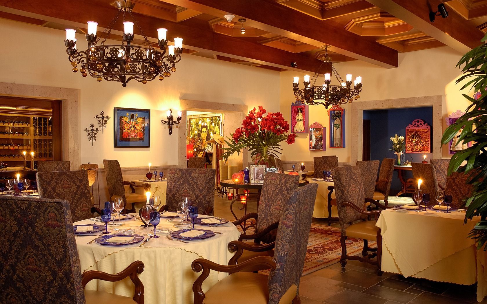Elegant restaurant dining room with chandeliers, wooden beams, and candlelit tables set with white tablecloths.