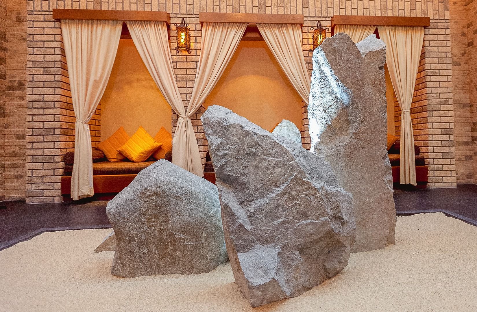 Rustic fireplace display with large gray rocks, cream curtains, and warm glowing firelight behind them