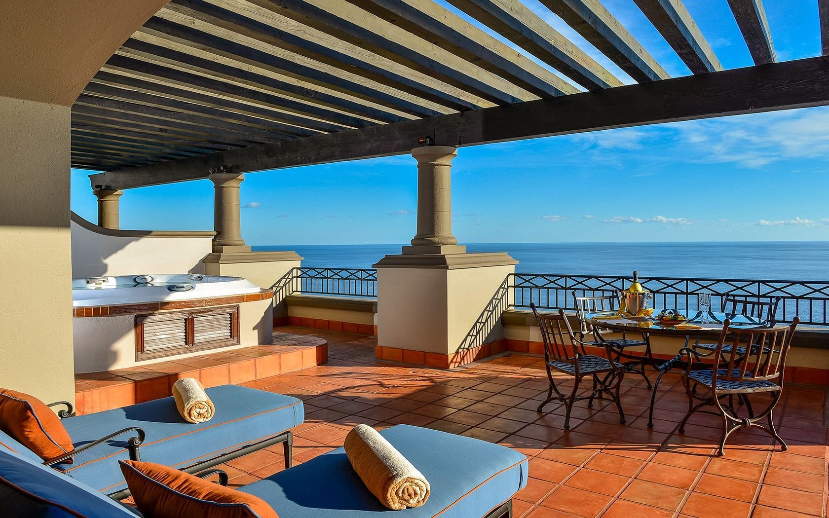 Rooftop terrace with lounge chairs, tables, and ocean view under a striped pergola