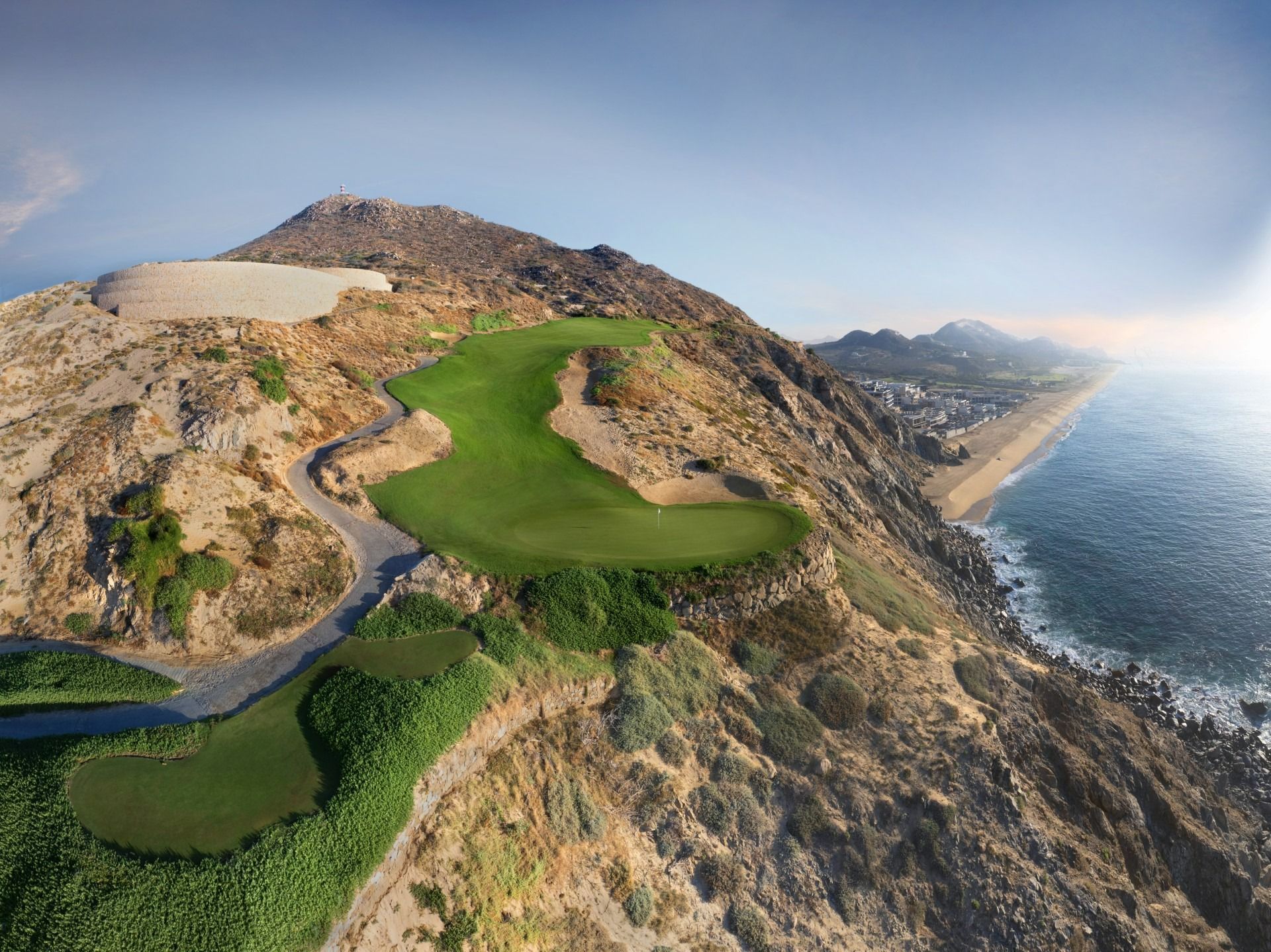 Coastal golf course fairway on a rocky cliff overlooking the ocean at sunset