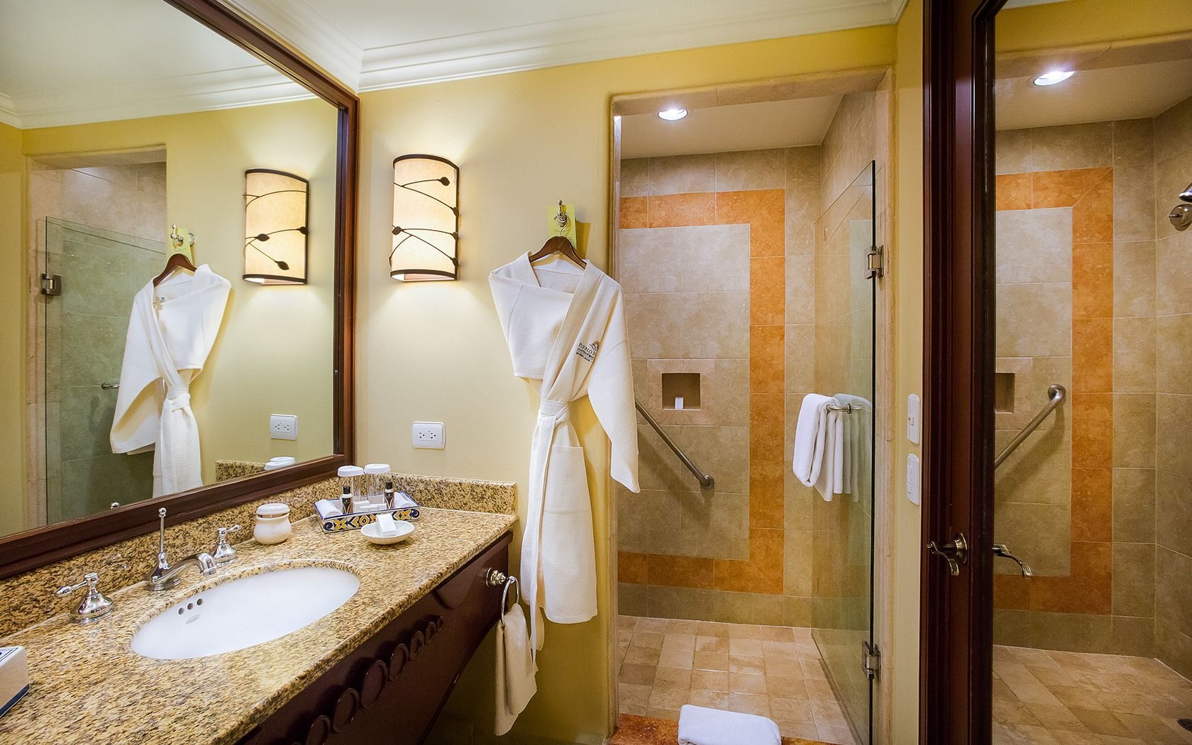 Elegant hotel bathroom with granite vanity, twin sinks, large mirror, and tiled shower area