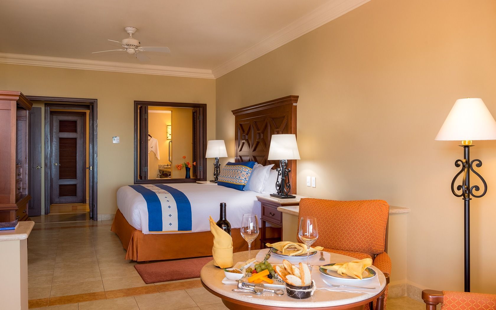 Hotel room with two beds, orange armchair, and breakfast tray beside a floor lamp