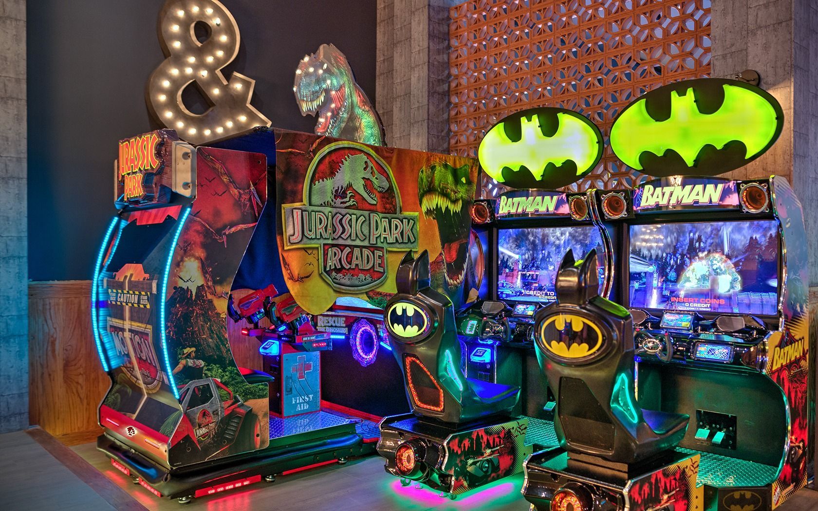 Colorful Batman-themed arcade machines glowing in a dark game room