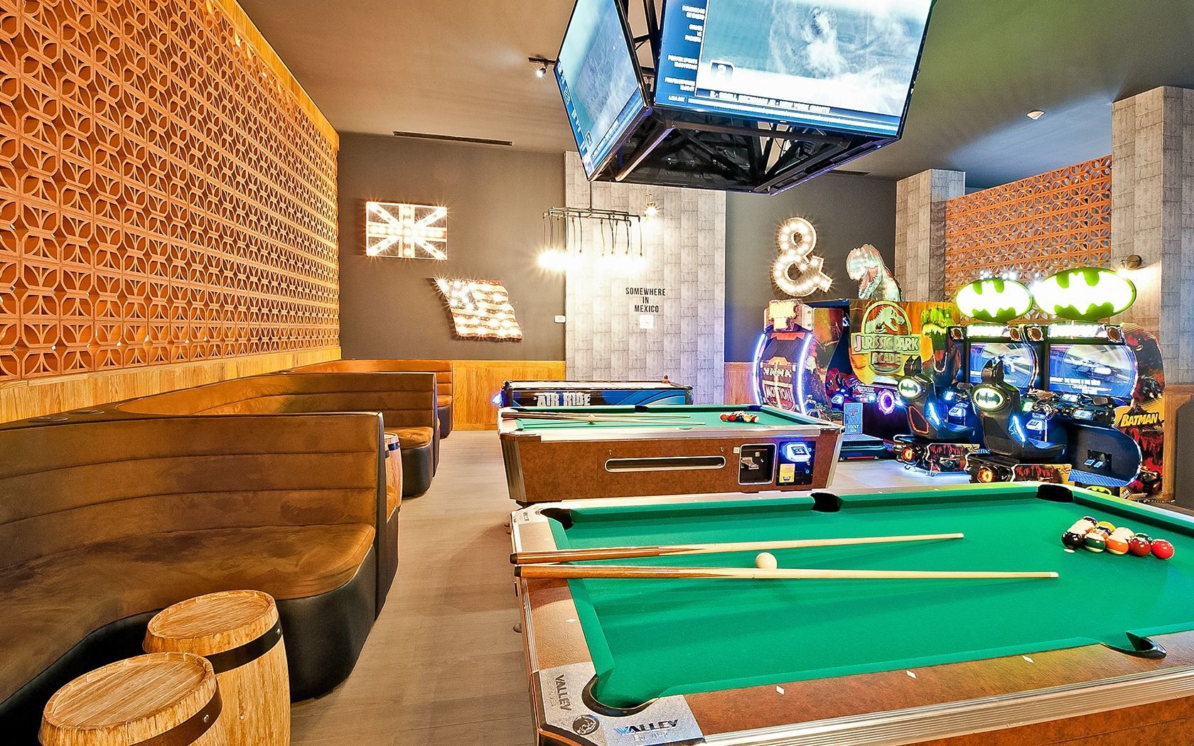 Pool hall with green-felt tables, wood-paneled booths, neon decor, and TV screens overhead