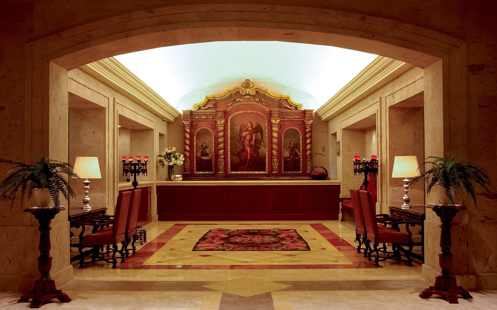 Elegant chapel altar with ornate gold panels, red carpet, and symmetrical candle stands in a warmly lit hall