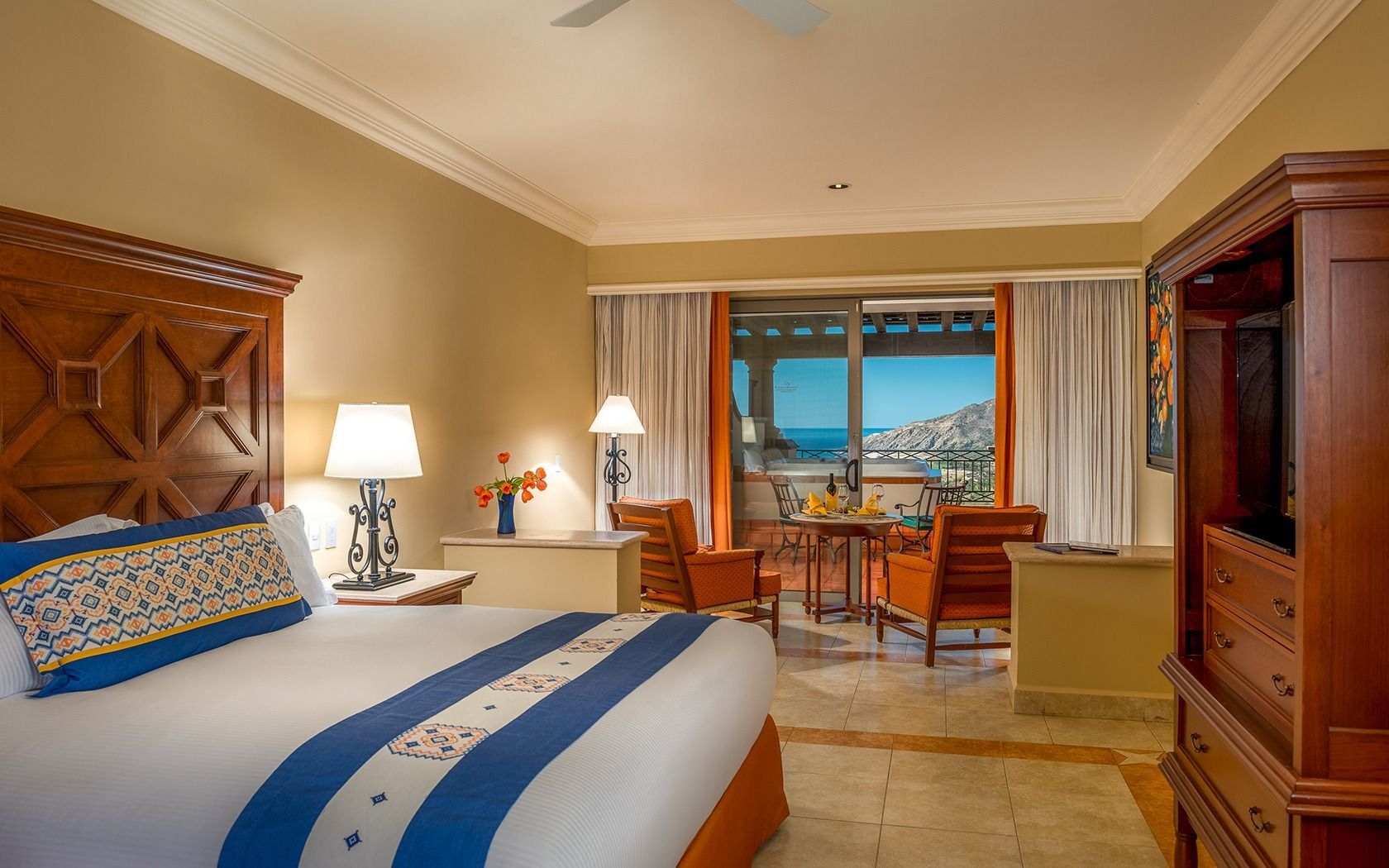 Hotel room with king bed, wooden furniture, and a balcony view of the ocean.