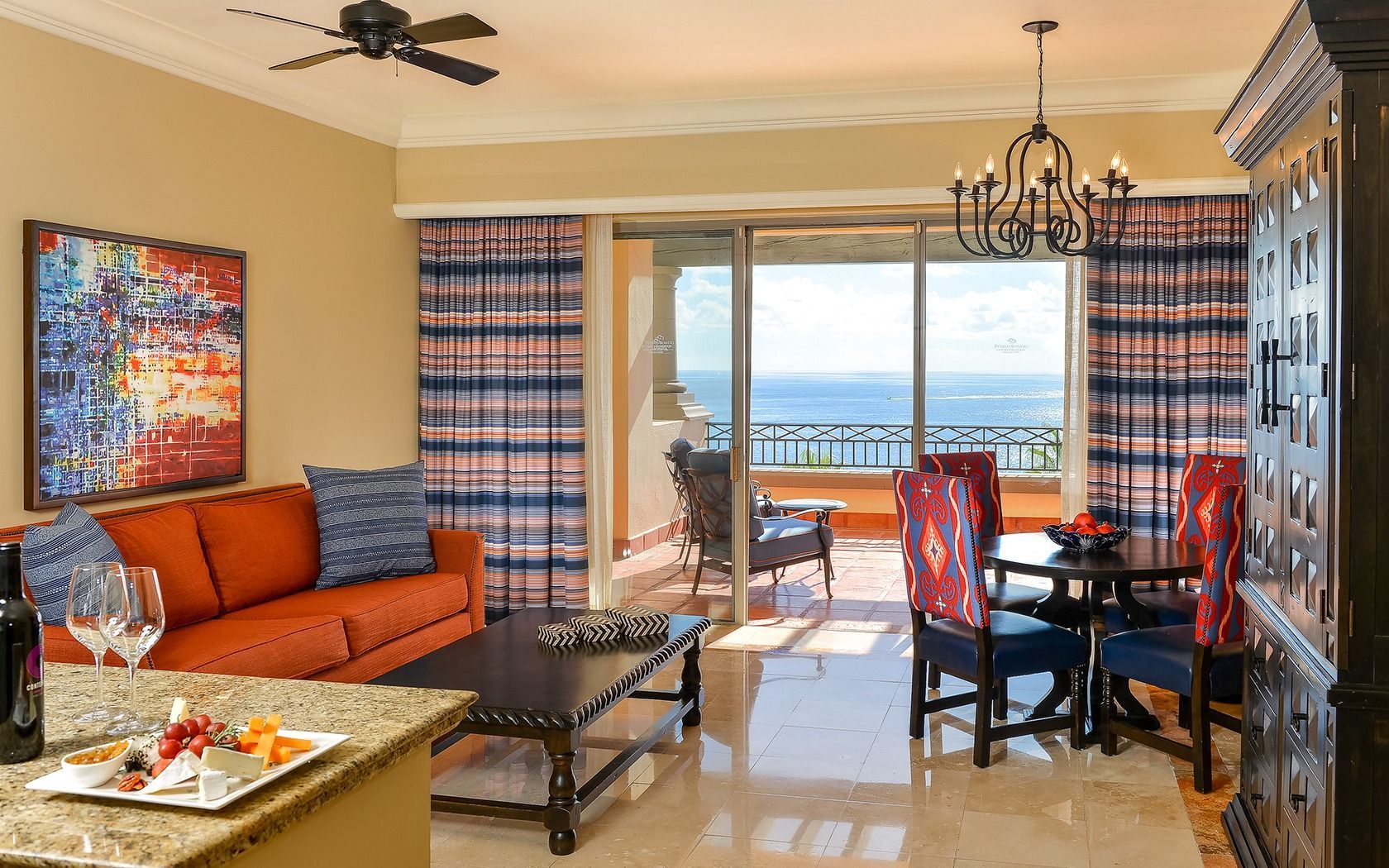 Bright living room with orange sofa, dining table, and ocean view through sliding glass doors.