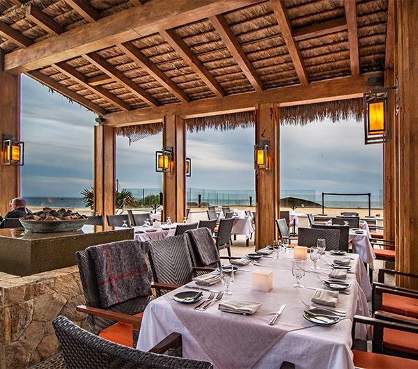 Open-air seaside restaurant with set tables, wooden beams, and ocean view