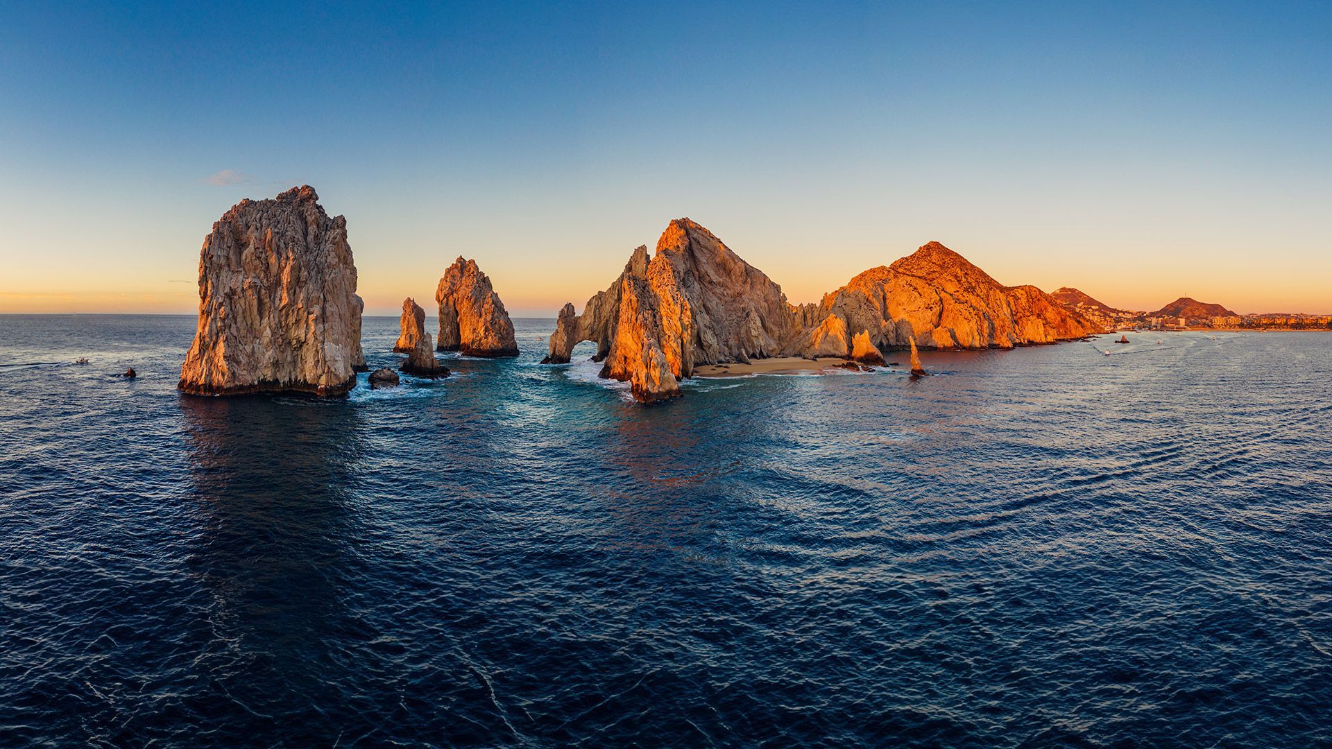 Rocky sea stacks rise from calm blue water under a partly cloudy sky.