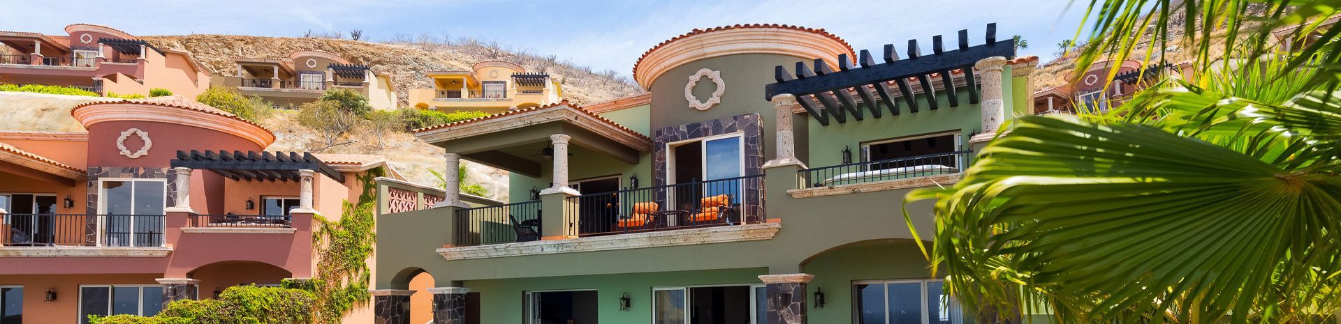 Colorful hillside resort buildings with balconies, tiled roofs, and palm fronds in front