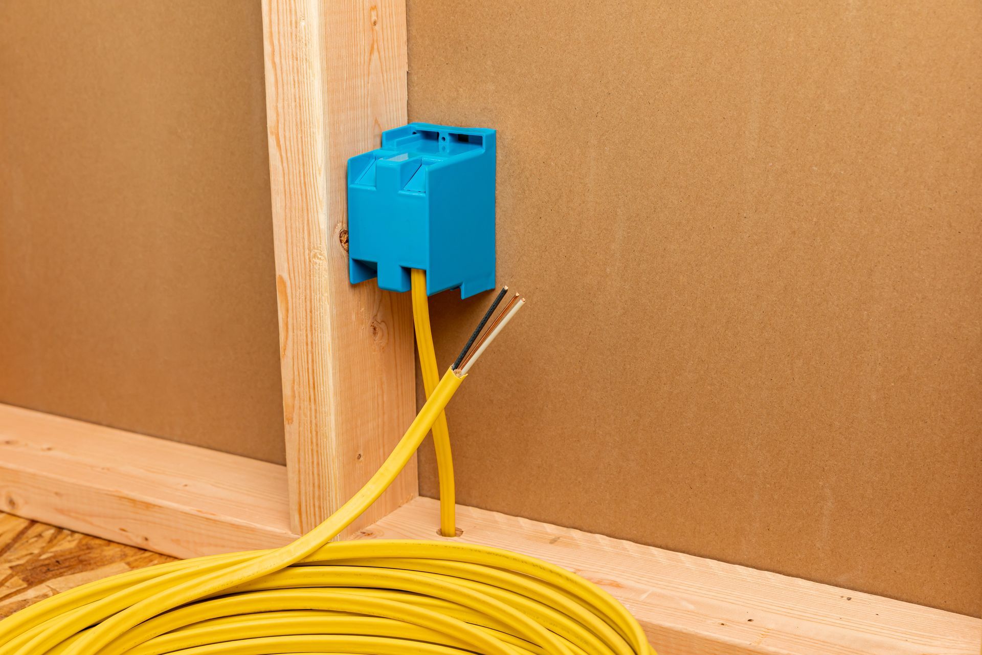 Gloved hands using wire strippers on electrical wires; blue, green, and brown exposed.