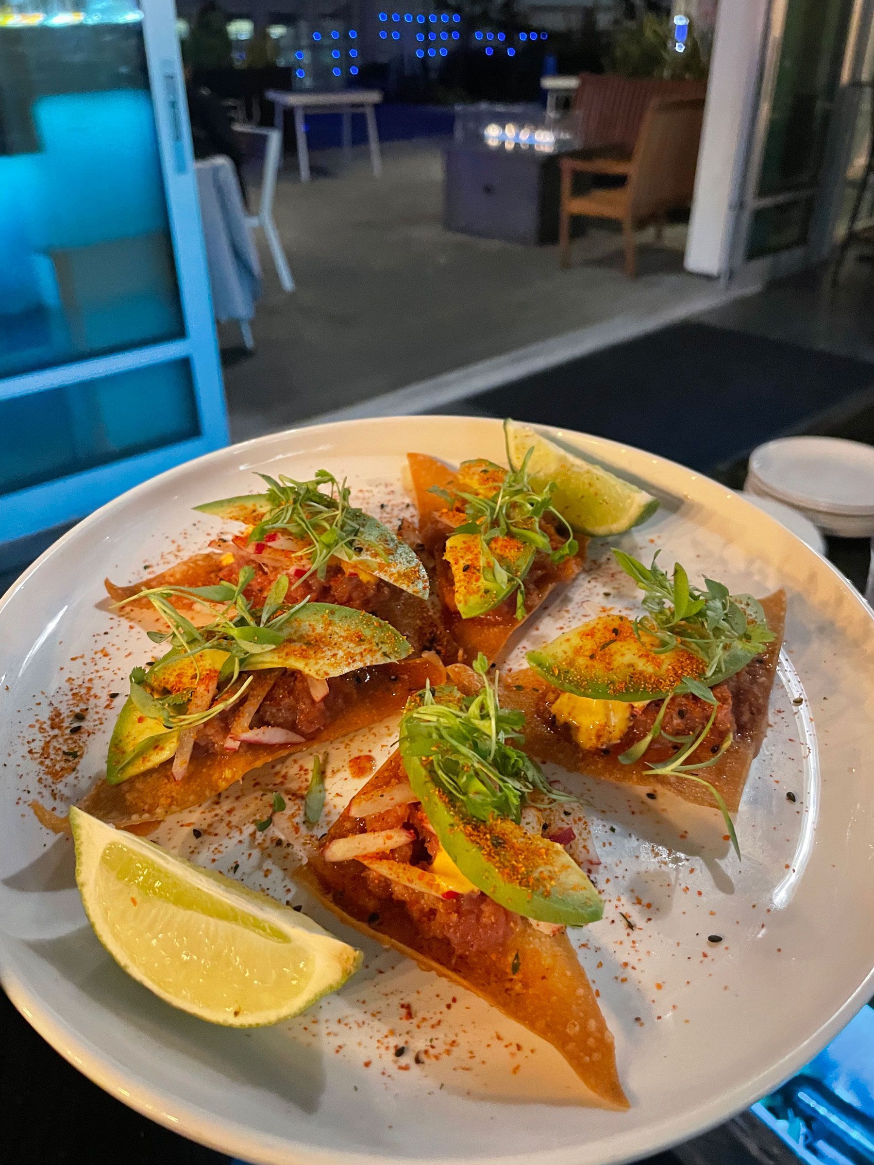 Plated tacos with lime wedges and herbs on a table in a dimly lit restaurant